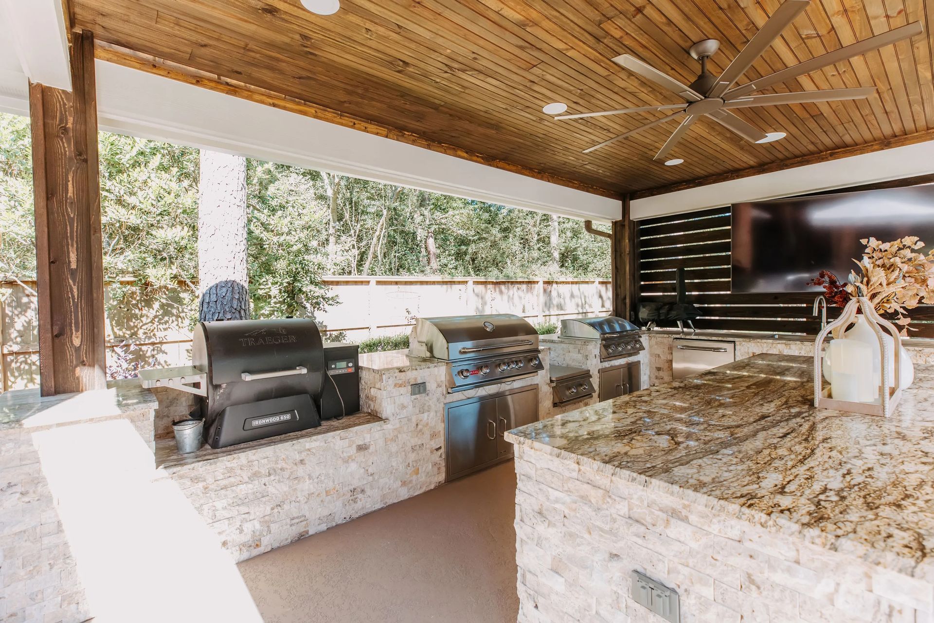 Outdoor kitchen with granite countertops, grill, and sink under a wood-paneled ceiling