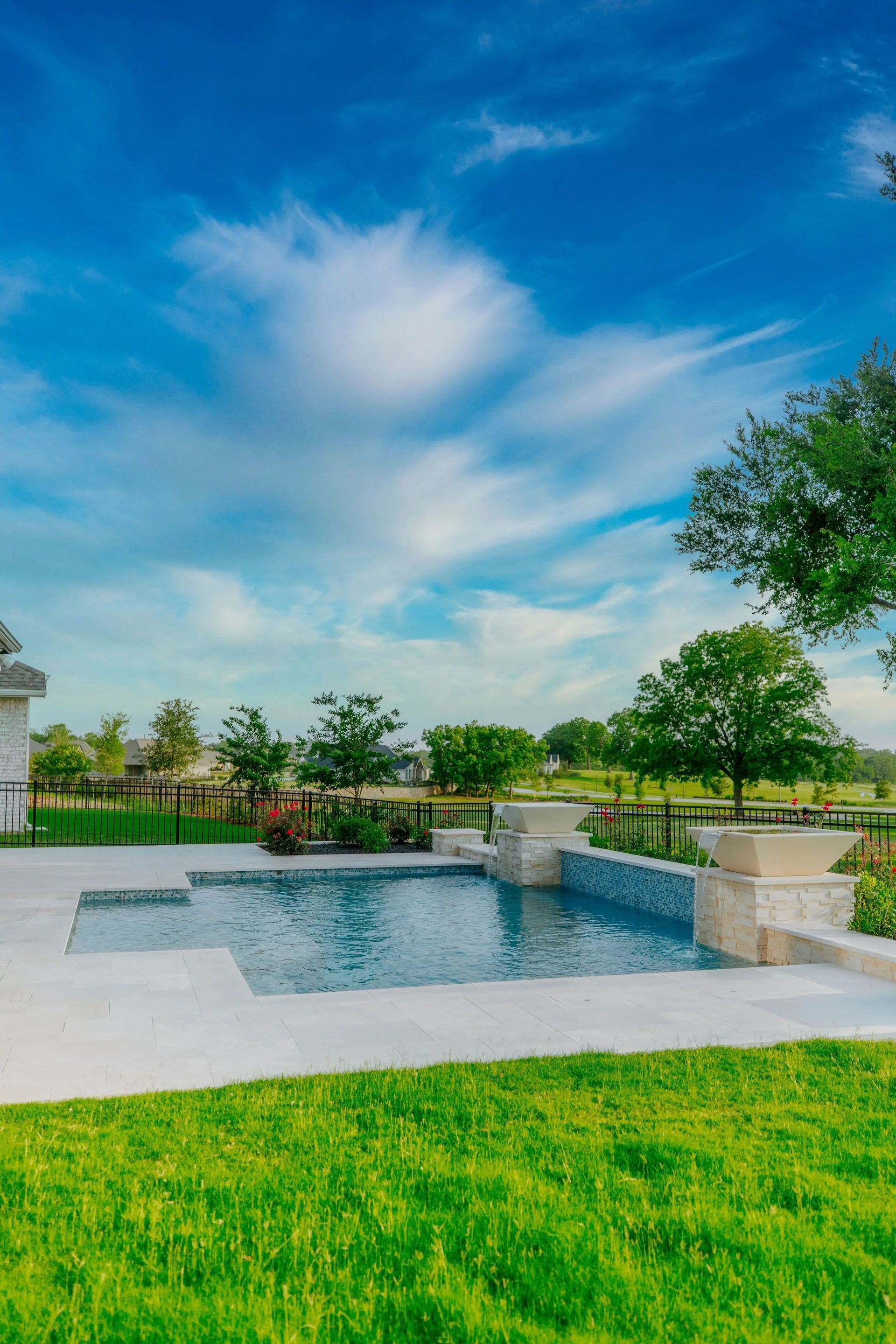 Sunny park with a small reflecting pool, green lawn, trees, and a blue sky with wispy clouds