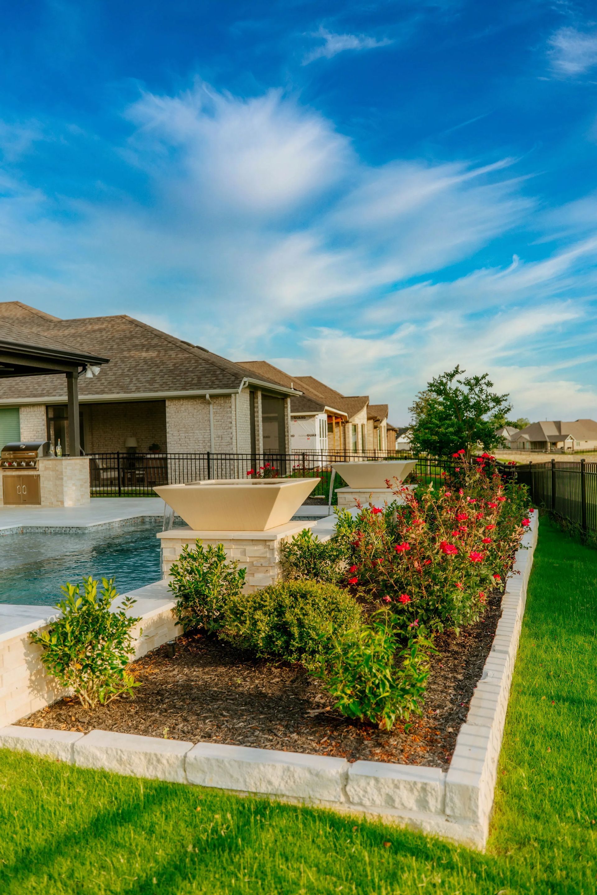 Suburban homes with a landscaped flower bed, fountain, and blue sky on a sunny day