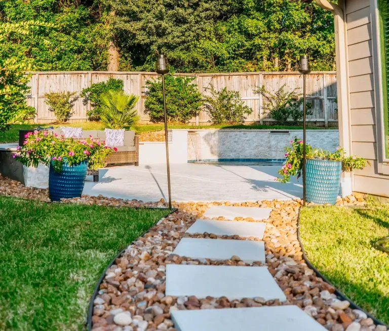 Sunny backyard garden with stepping-stone path, potted flowers, and raised planter beds