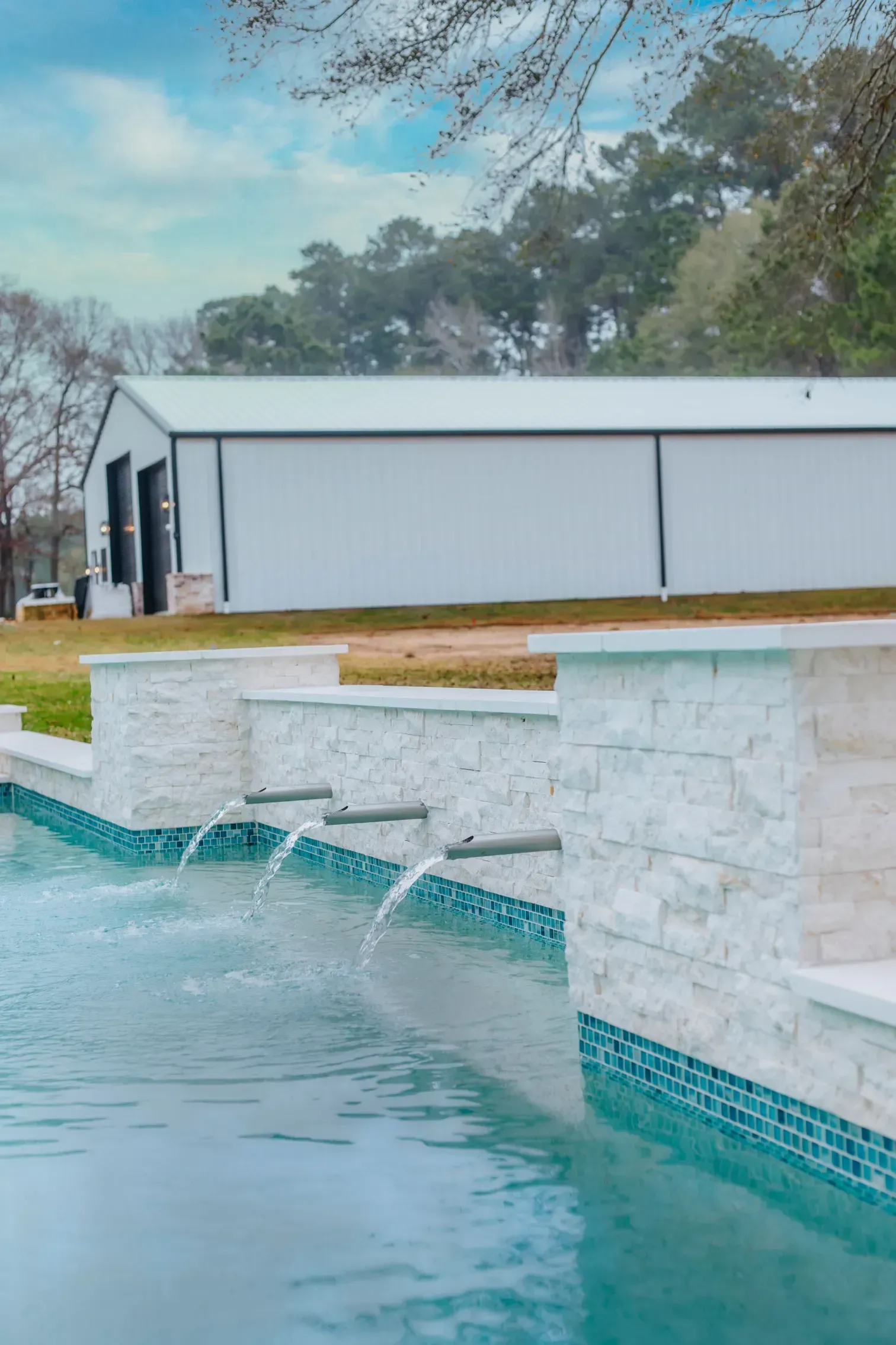 Modern pool with turquoise water, stone waterfall wall, and a white building in the background