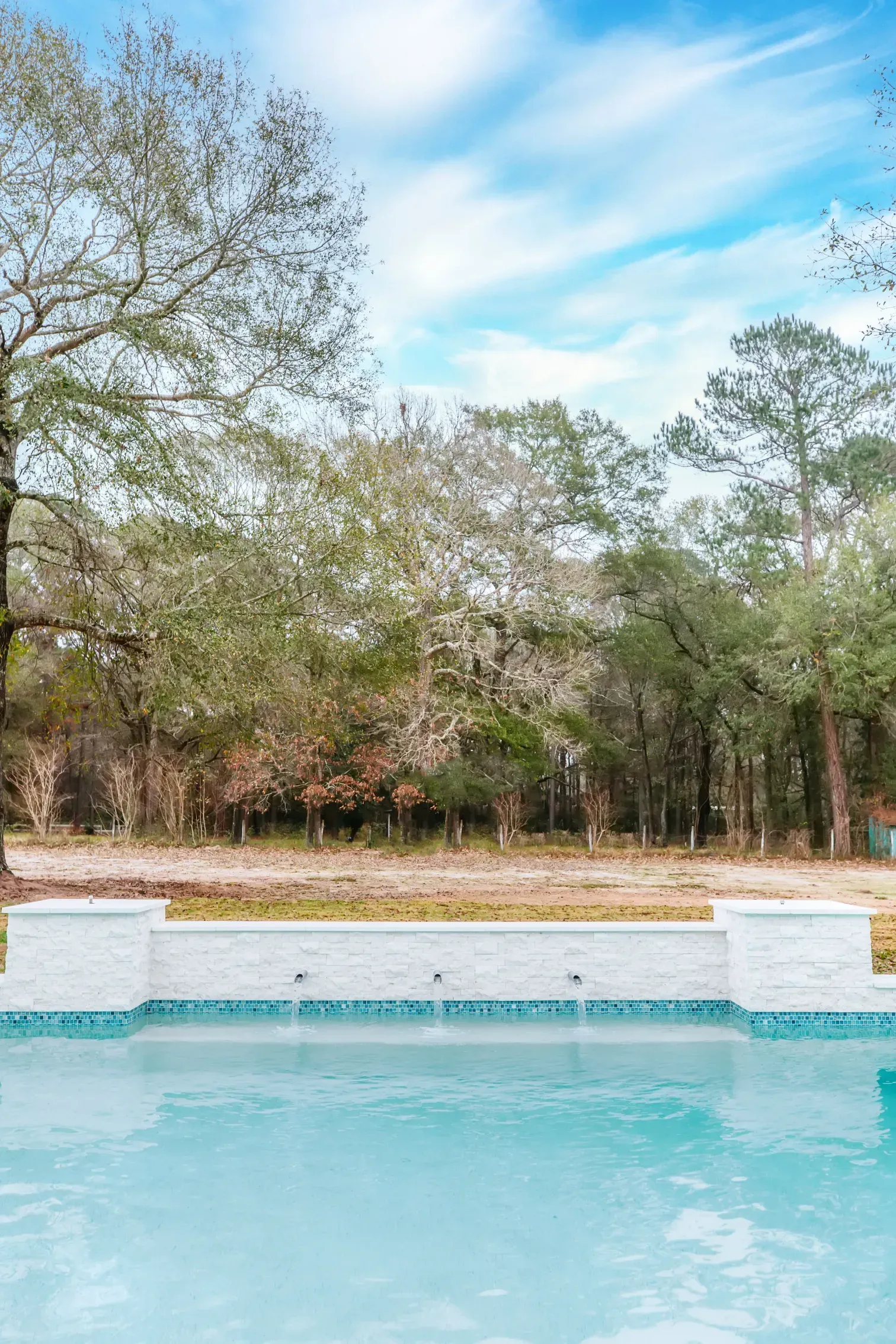 Blue swimming pool beside trees under a partly cloudy sky