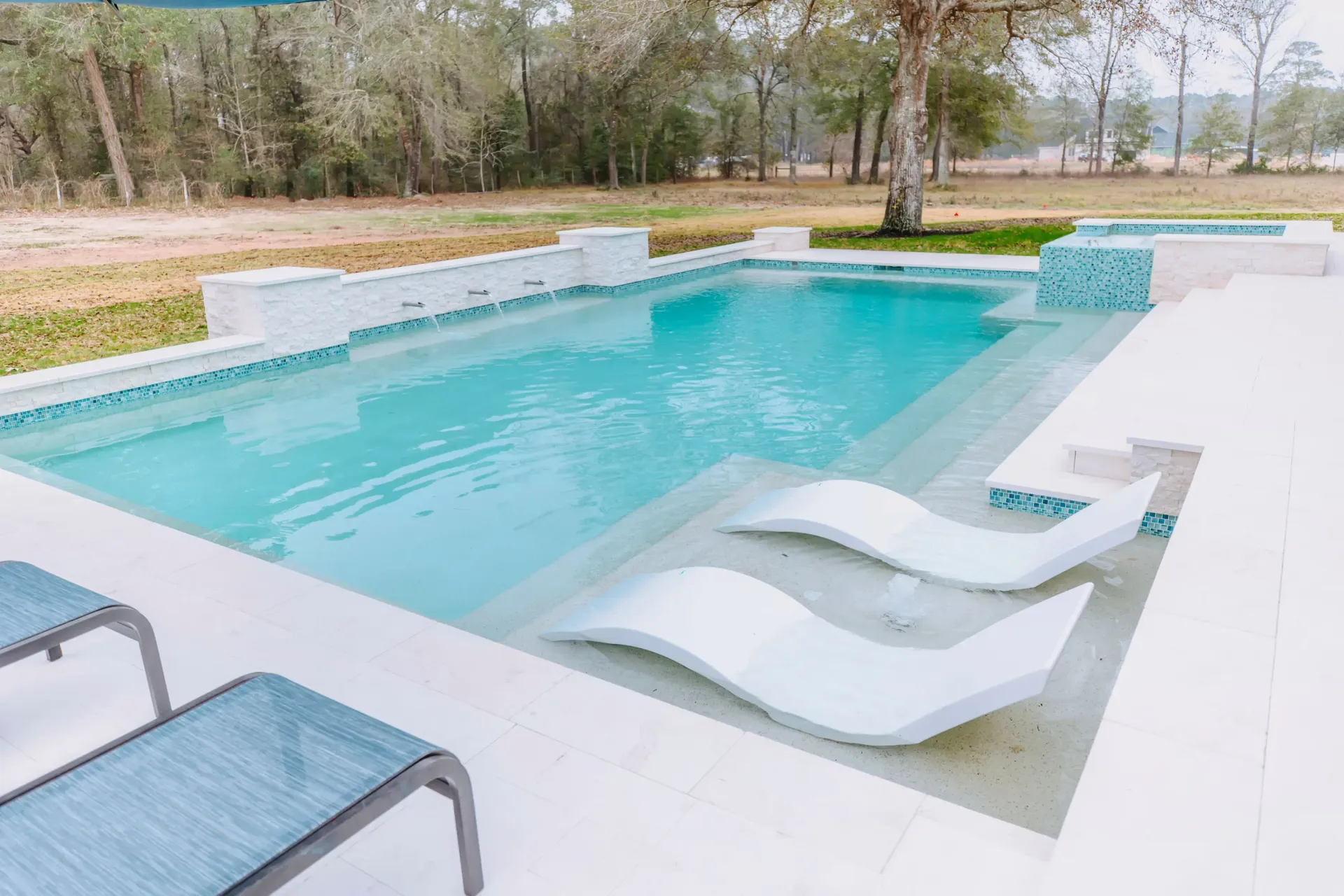 Modern outdoor swimming pool with white loungers and trees in the background