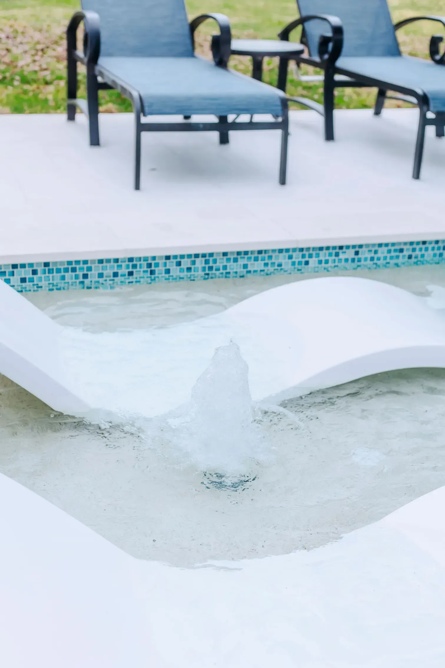 Outdoor pool deck with lounge chairs beside an empty, covered pool basin with a curved white liner.
