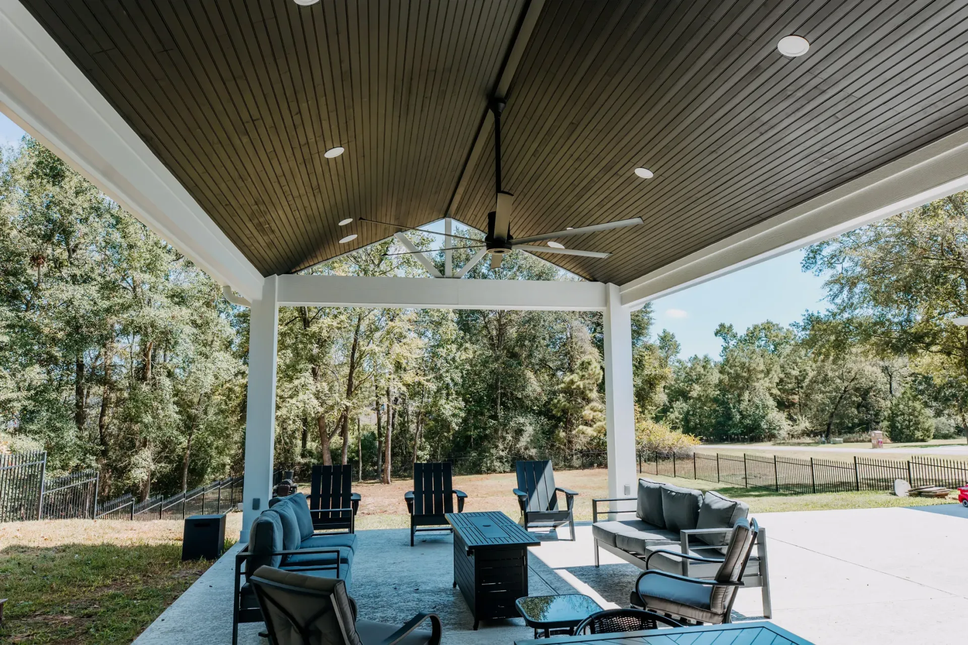 Covered outdoor patio with white columns, blue chairs, and tables overlooking a wooded yard