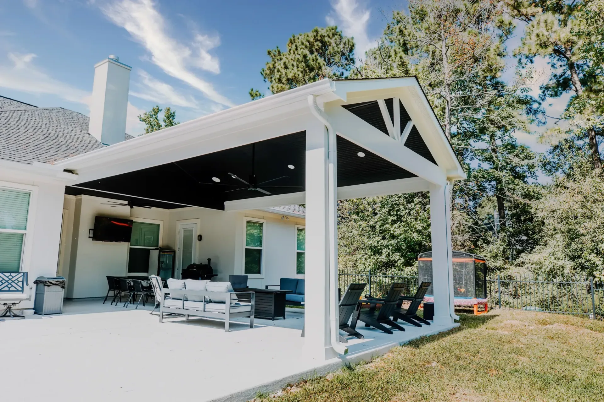 Modern white patio pavilion with seating and a grassy yard, surrounded by trees