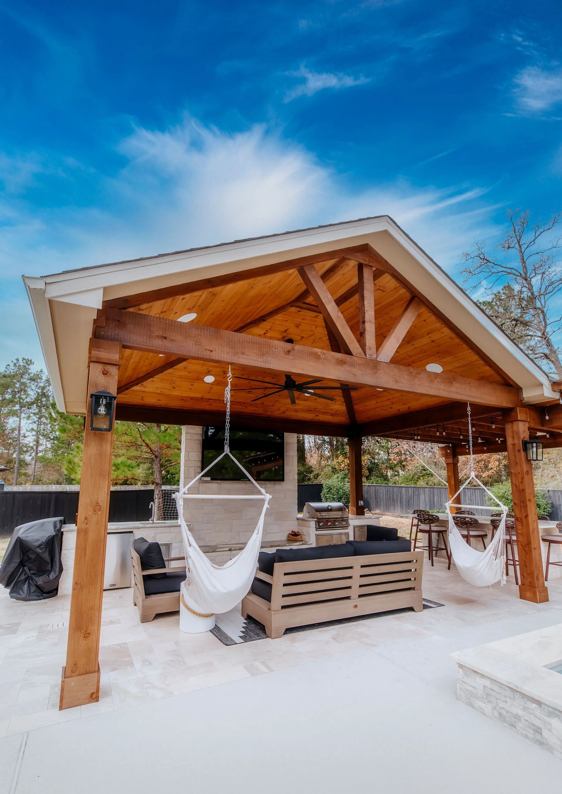 Snow-covered wooden gazebo with hanging chairs and a hot tub under a blue sky