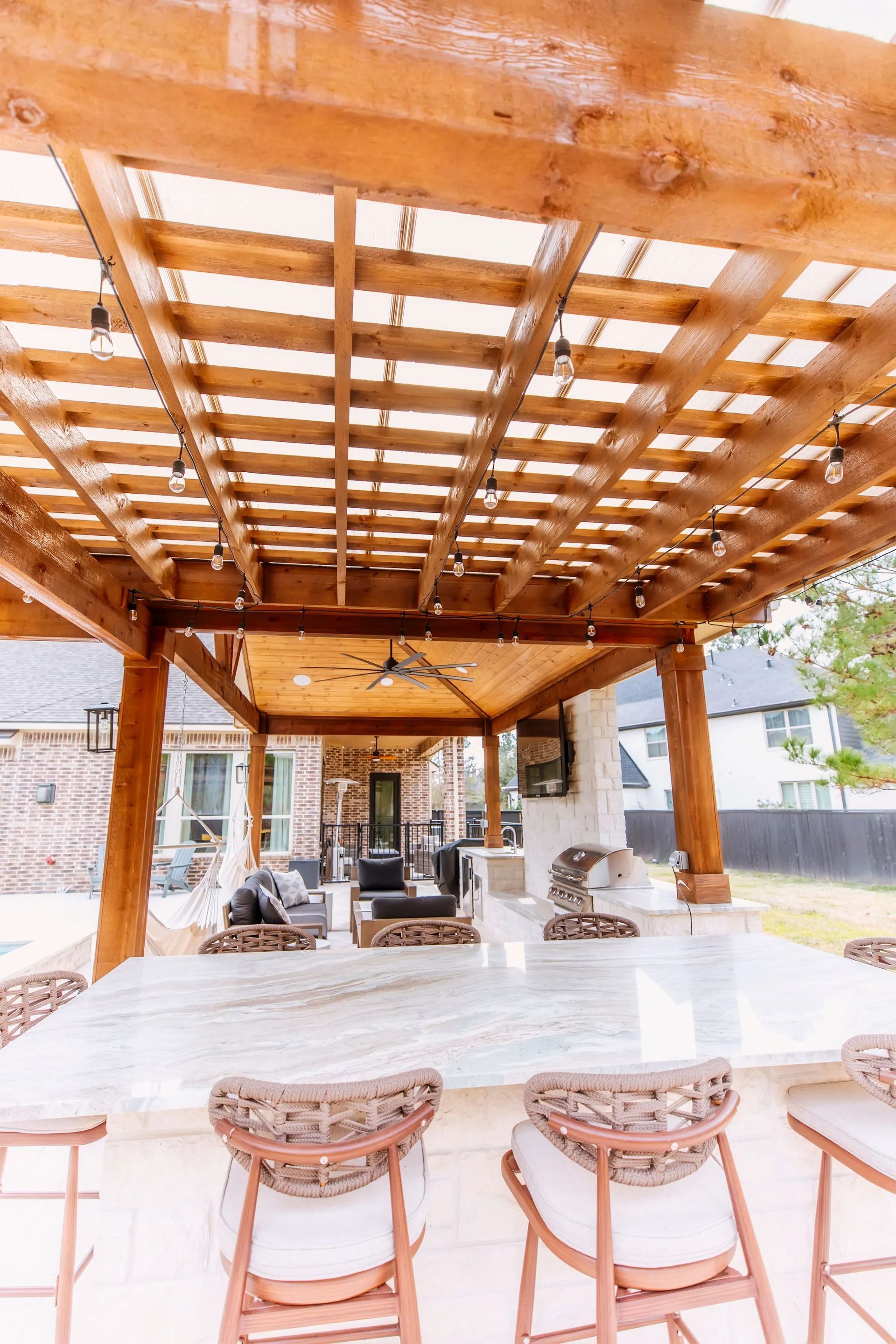 Wooden pergola over a modern outdoor patio with wicker chairs and a long table