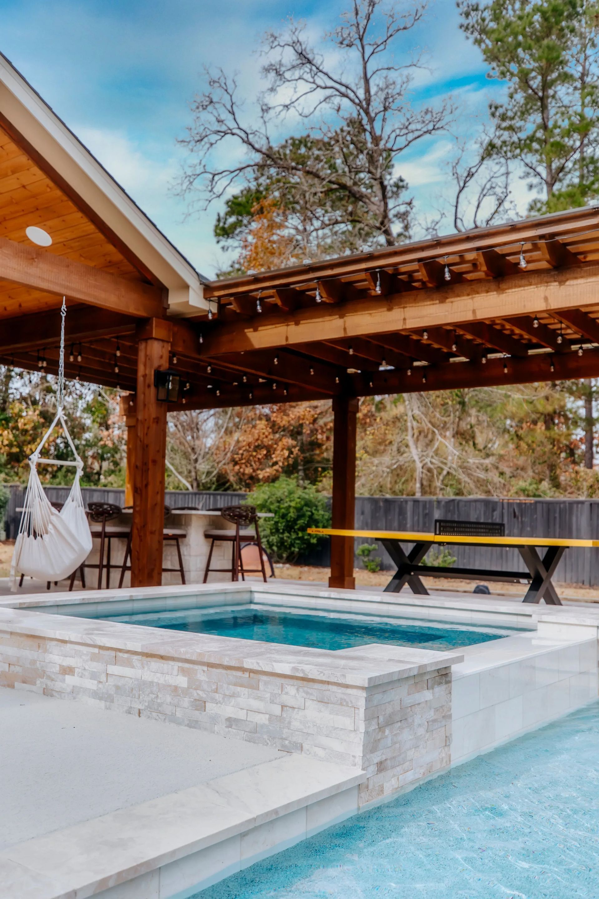 Modern patio with a small pool, wooden pergola, and lounge chairs under a blue sky