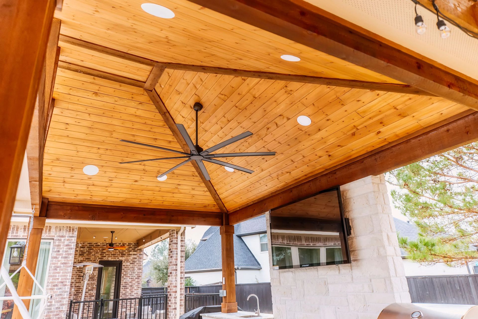 Covered wooden patio ceiling with a large black ceiling fan and recessed lights
