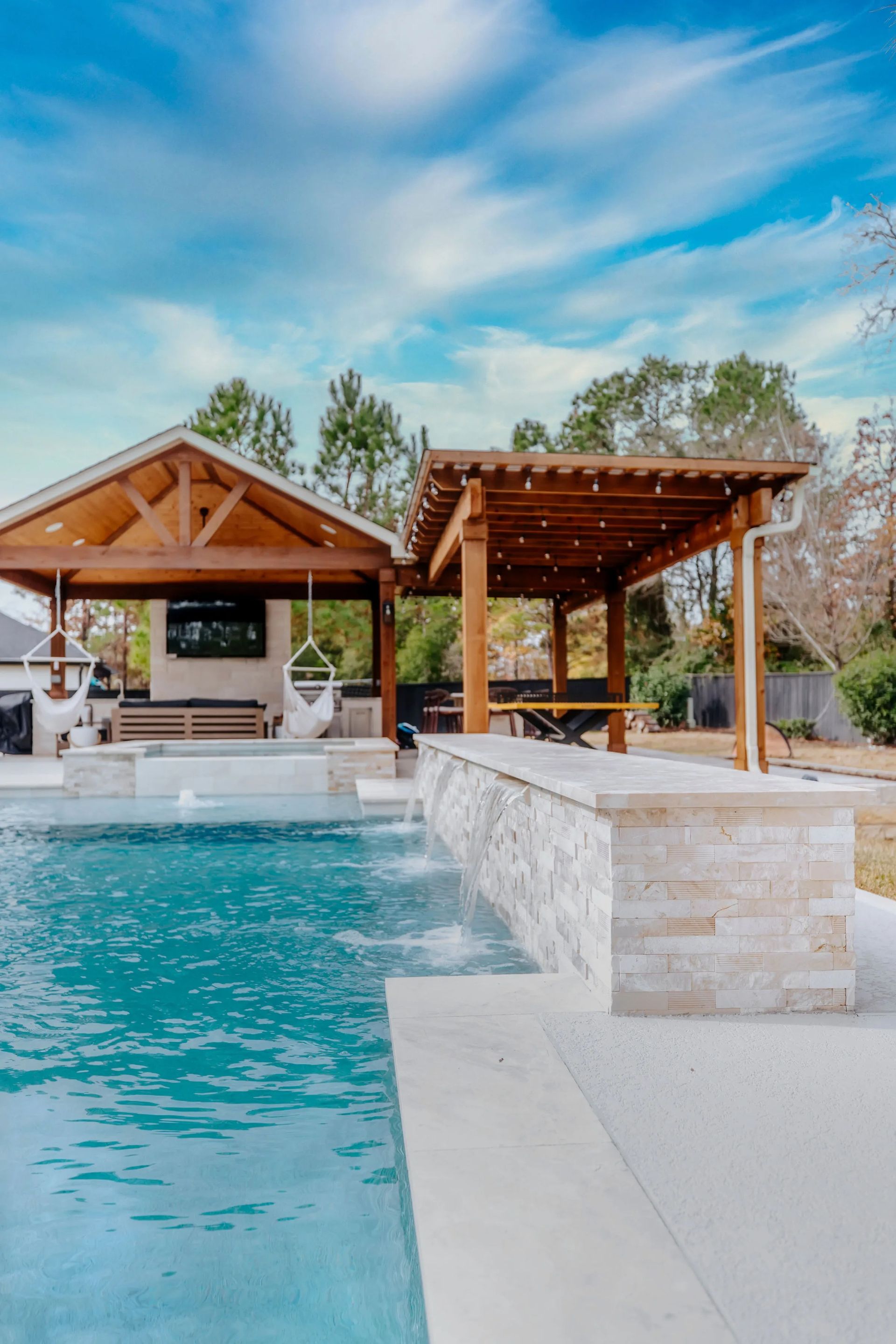 Luxury backyard pool with stone bar, wood pergolas, and turquoise water under a blue sky