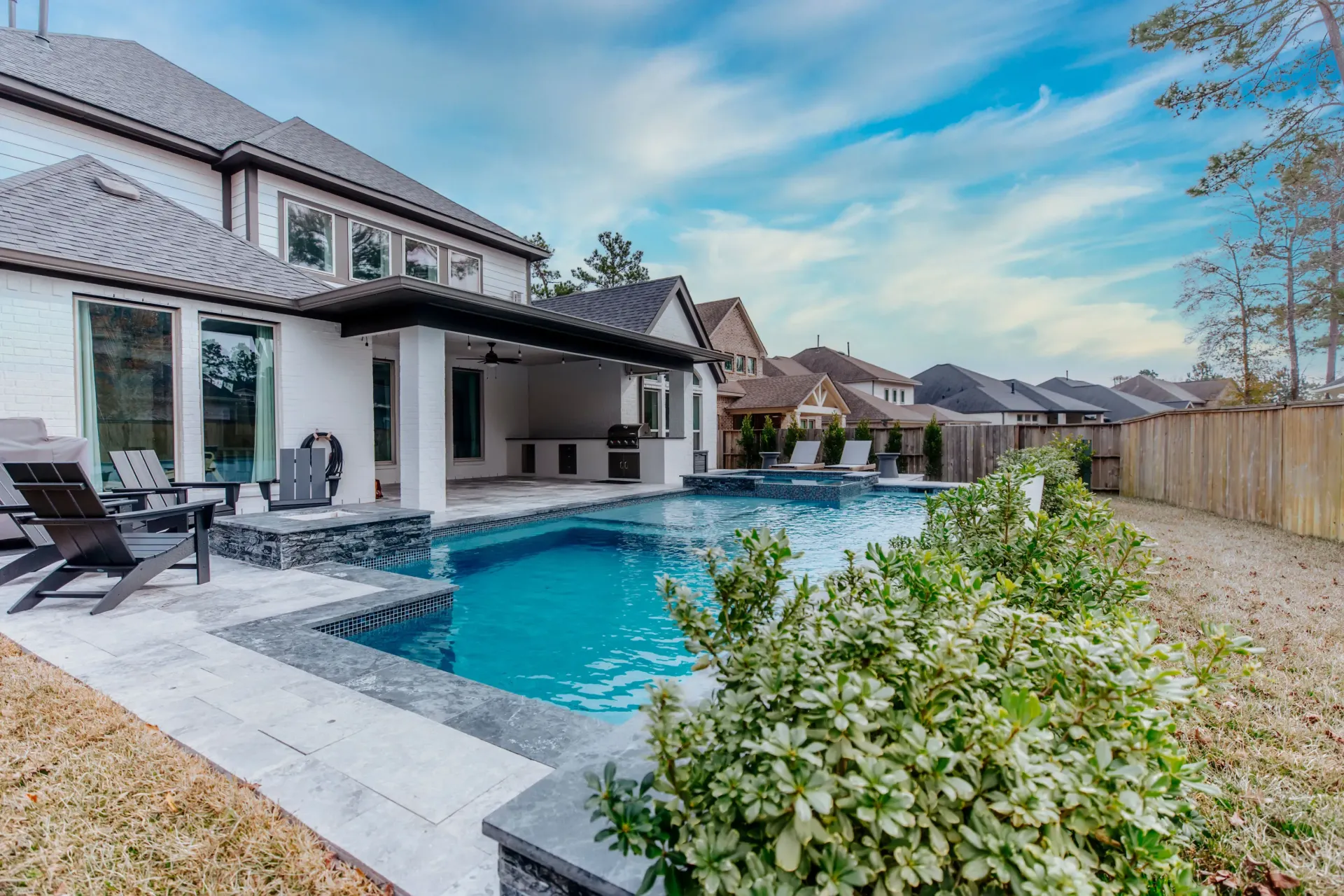 Backyard swimming pool beside a modern house with patio seating and a landscaped fence line
