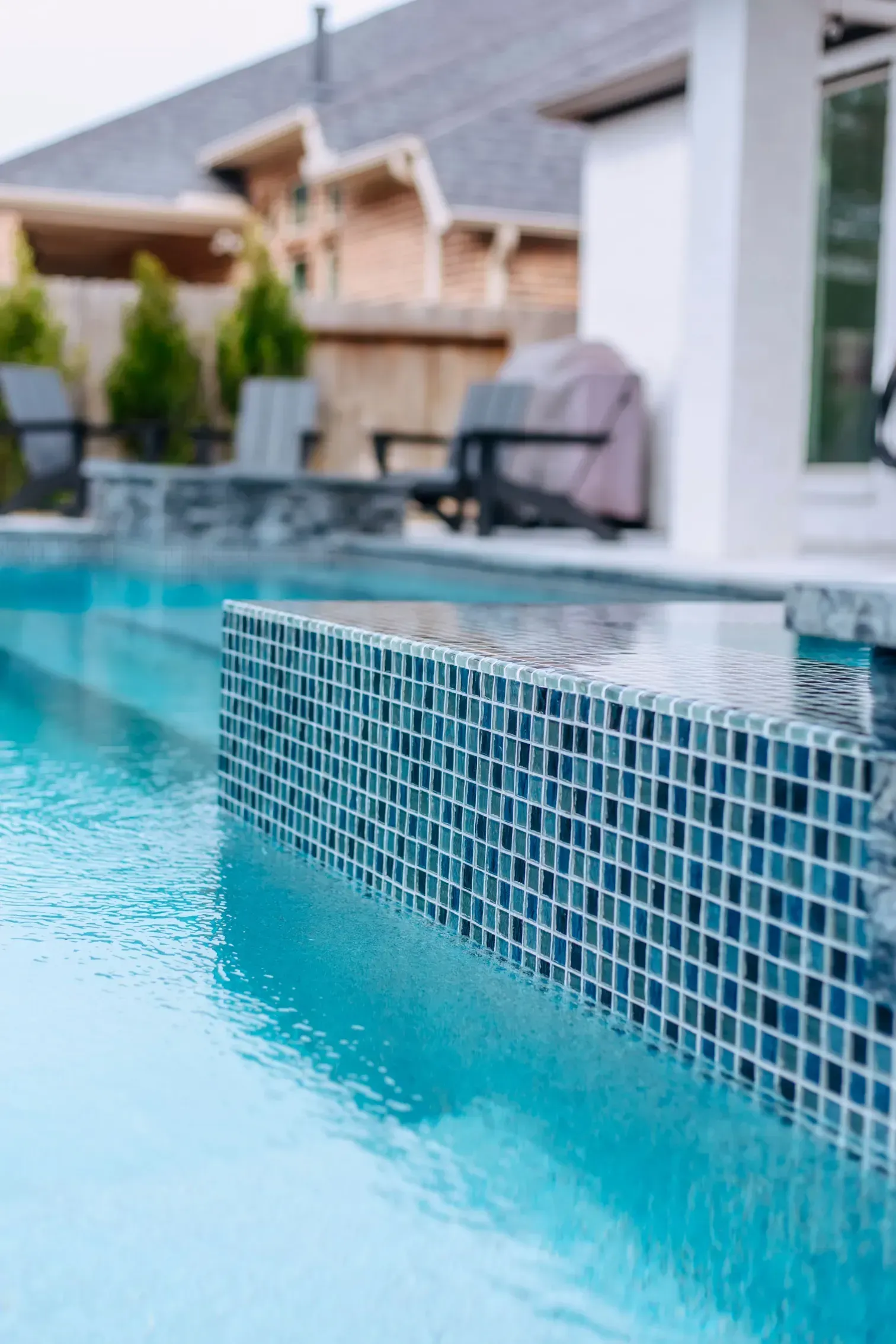 Close-up of a turquoise swimming pool with blue mosaic tile edging in a backyard setting