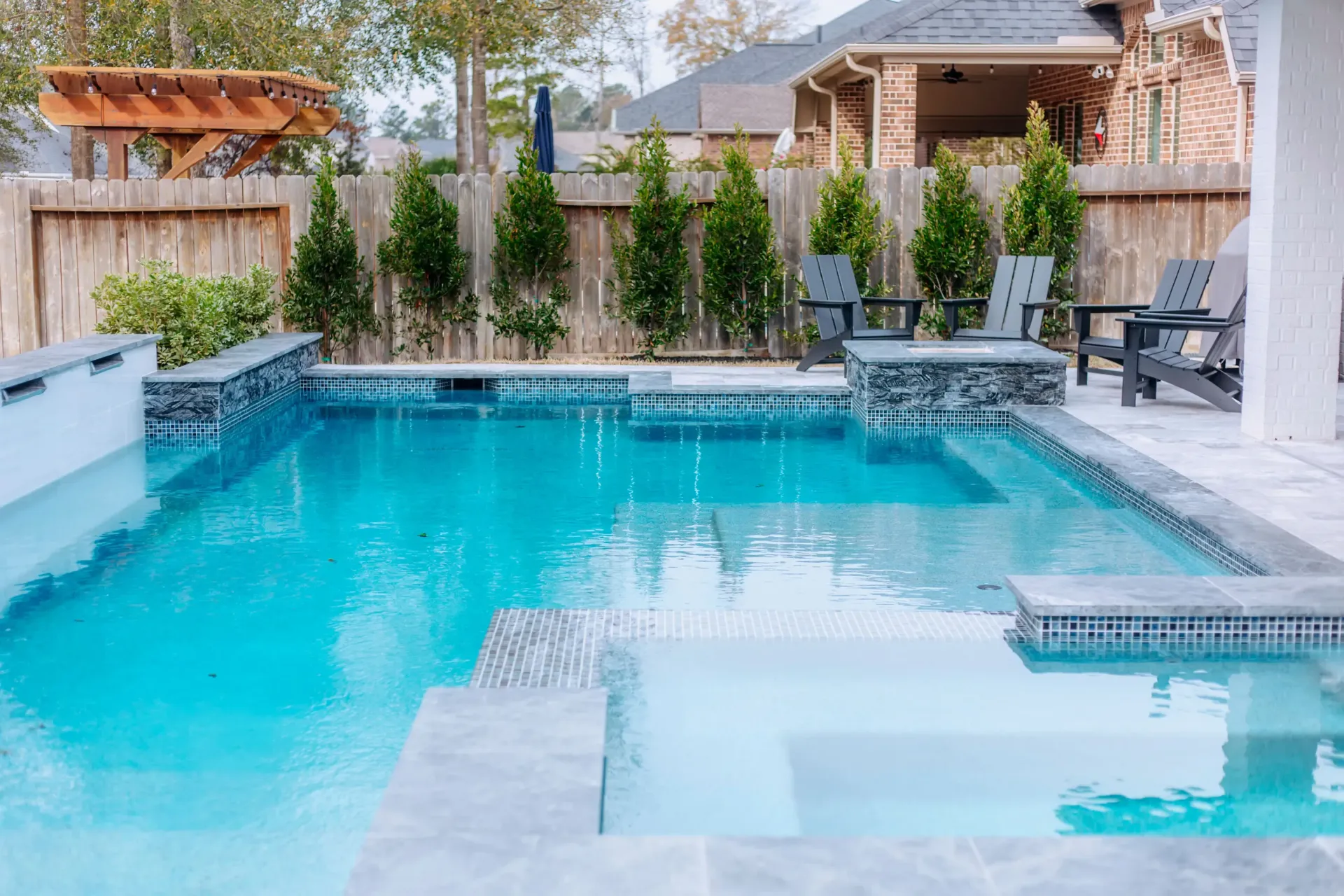 Backyard swimming pool with turquoise water, stone coping, lounge chairs, and a hot tub area