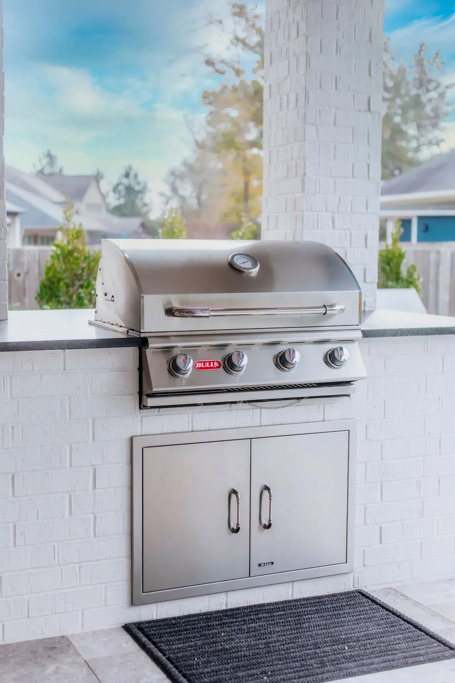 Built-in stainless steel outdoor grill set into a white brick patio wall