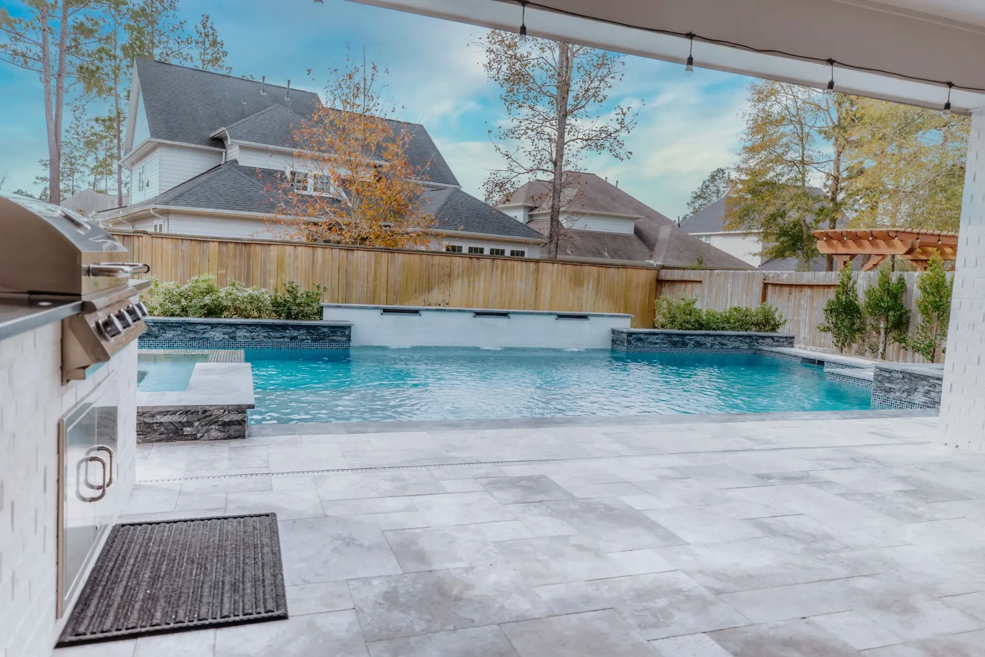 Covered patio overlooking a backyard pool and spa, with houses and a wooden fence beyond.
