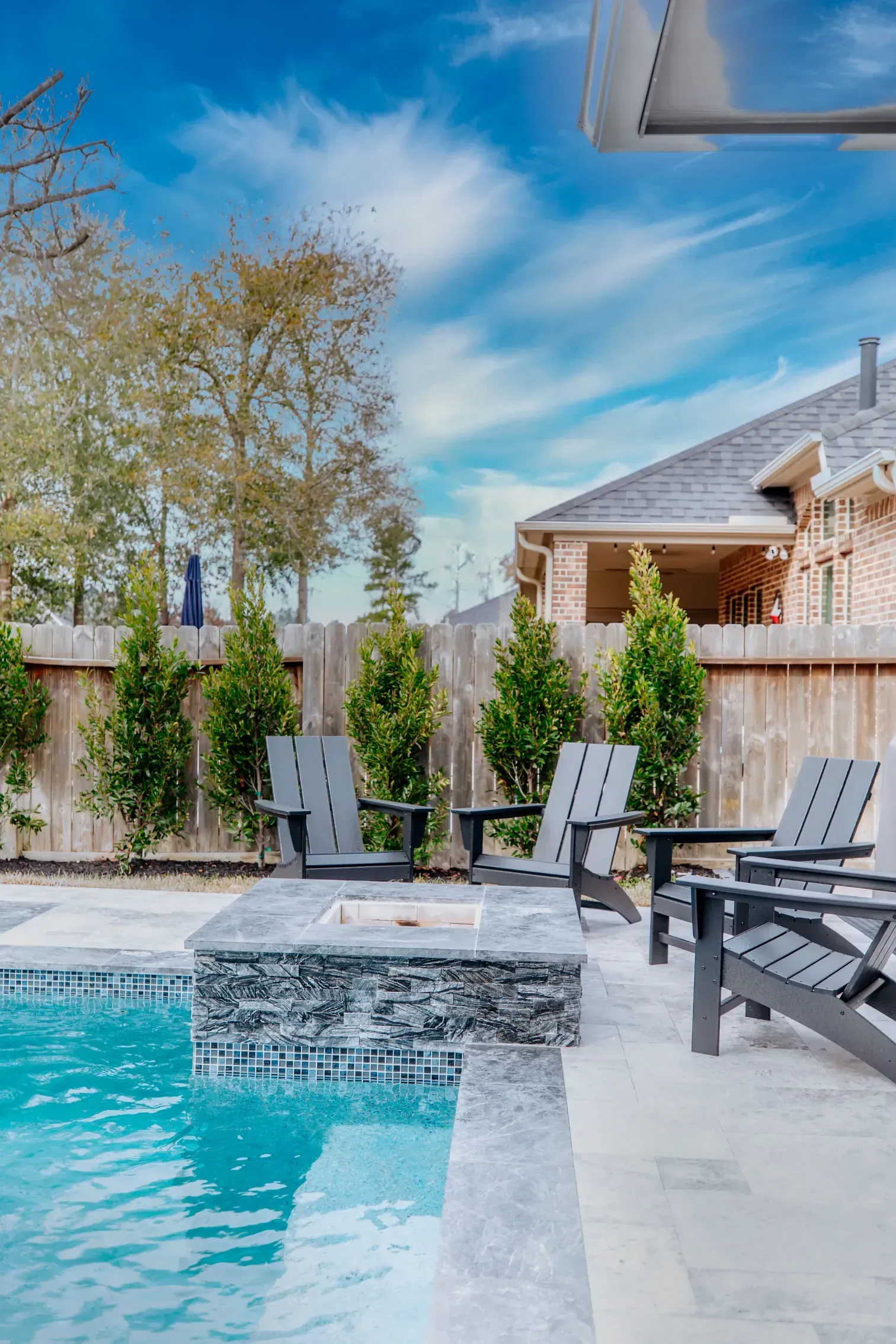 Backyard pool with lounge chairs, stone patio, and a blue sky