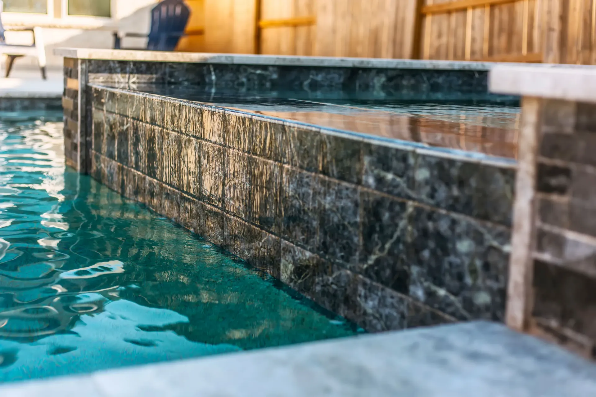 Turquoise pool water beside a dark tiled spa edge and wooden fence