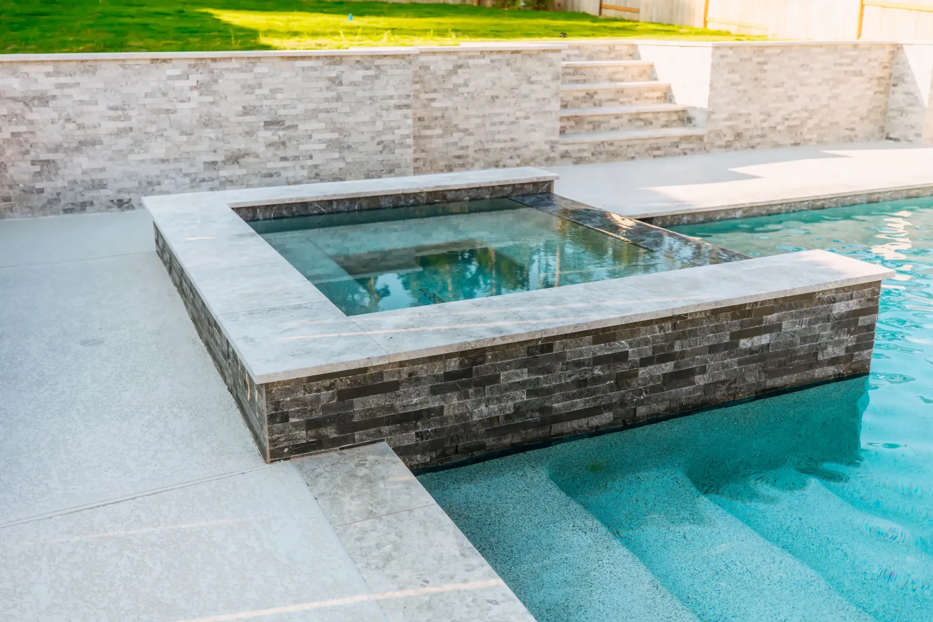 Modern backyard pool with raised stone spa and turquoise water