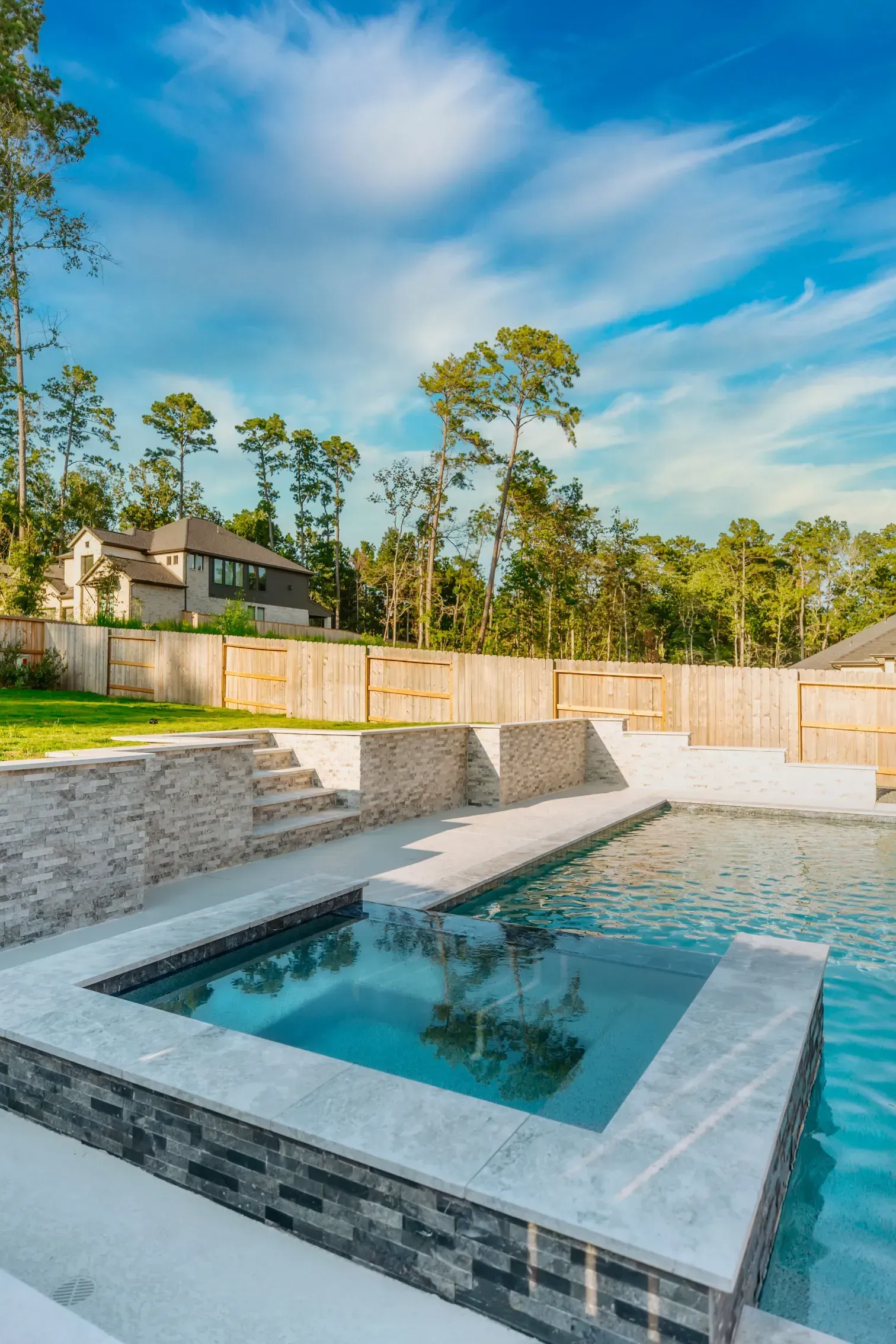 Modern backyard pool with waterfall ledge, stone decking, and blue sky backdrop