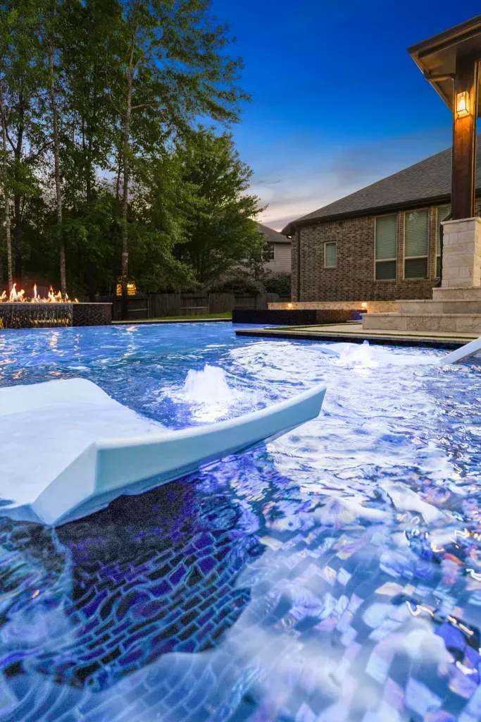 Luxury backyard pool at dusk with blue water, loungers, and a modern house beside trees