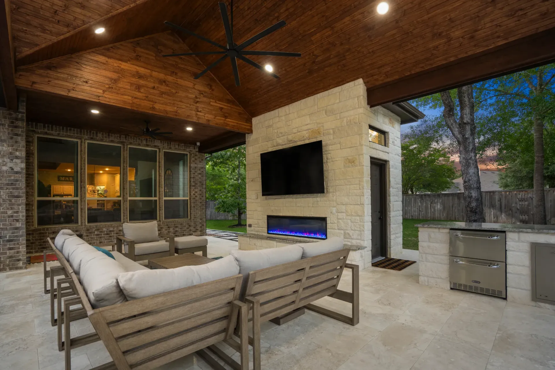 Covered outdoor patio with sectional seating, TV, fireplace, and built-in grill under a wood ceiling