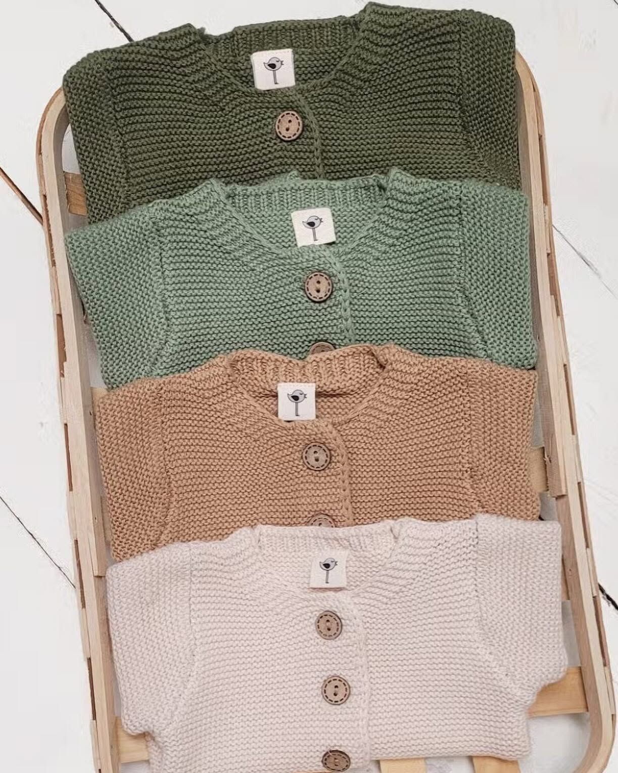 Stacked knit cardigans in olive, sage, beige, and cream on a rack