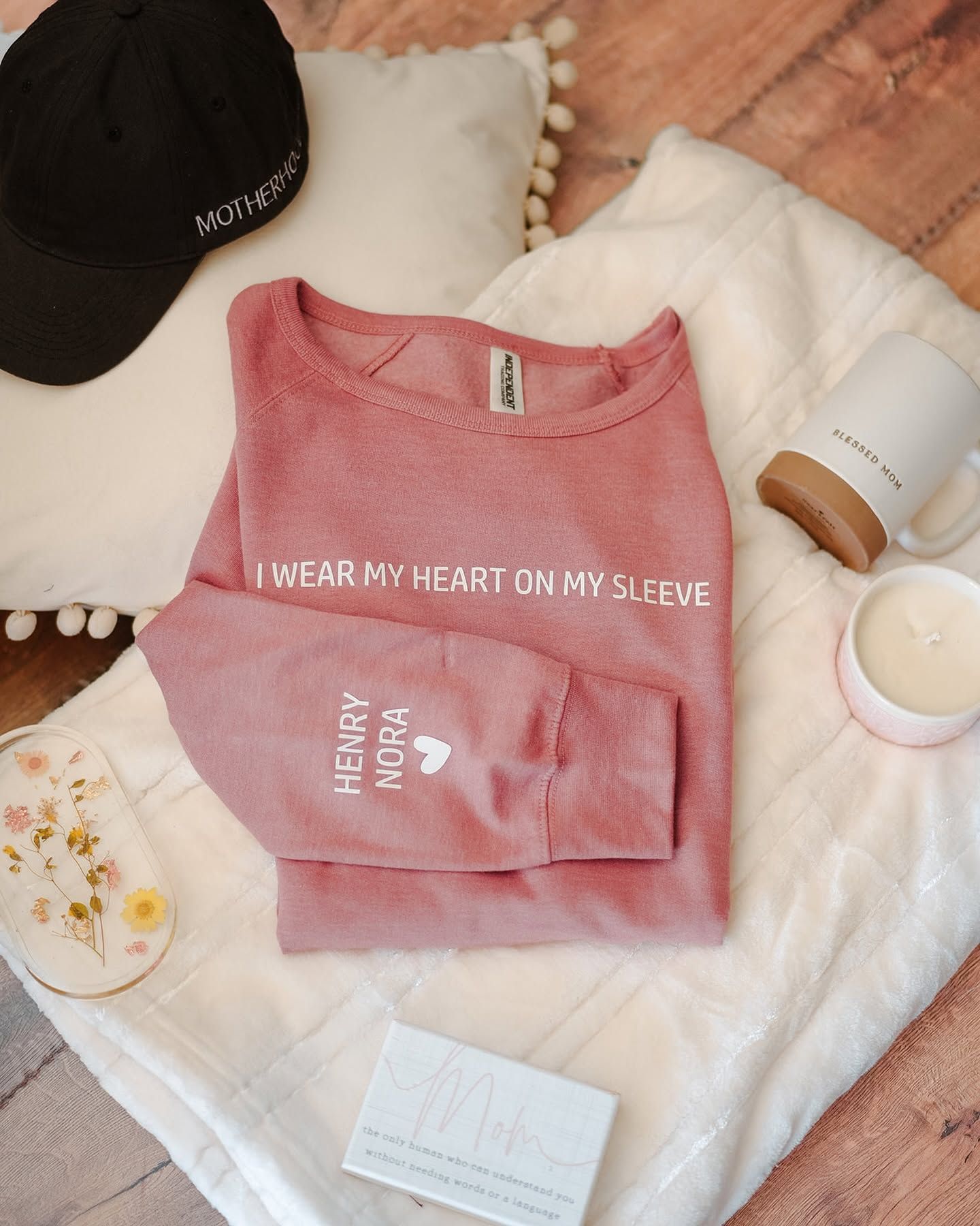 Pink loungewear set on a white blanket with a black cap, candles, and flowers nearby.