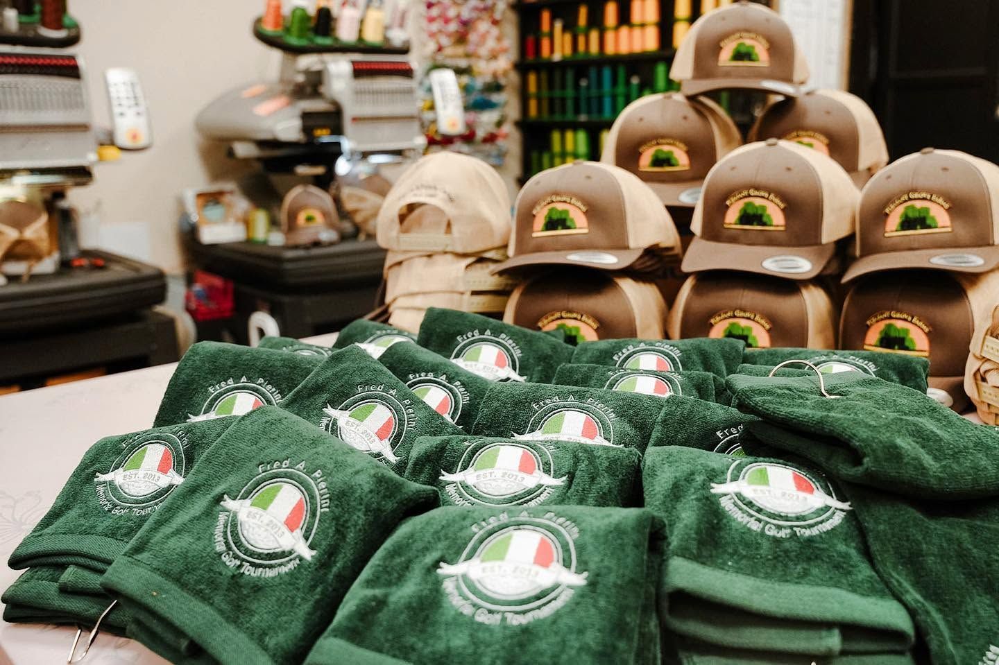 Stacks of green and tan caps with embroidered logos displayed on a store counter