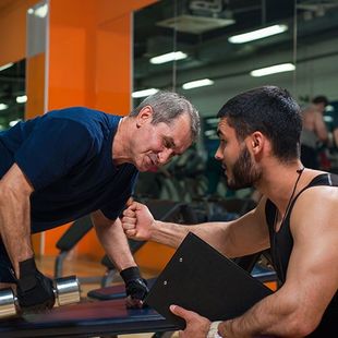 A man is talking to another man in a gym while holding a clipboard.