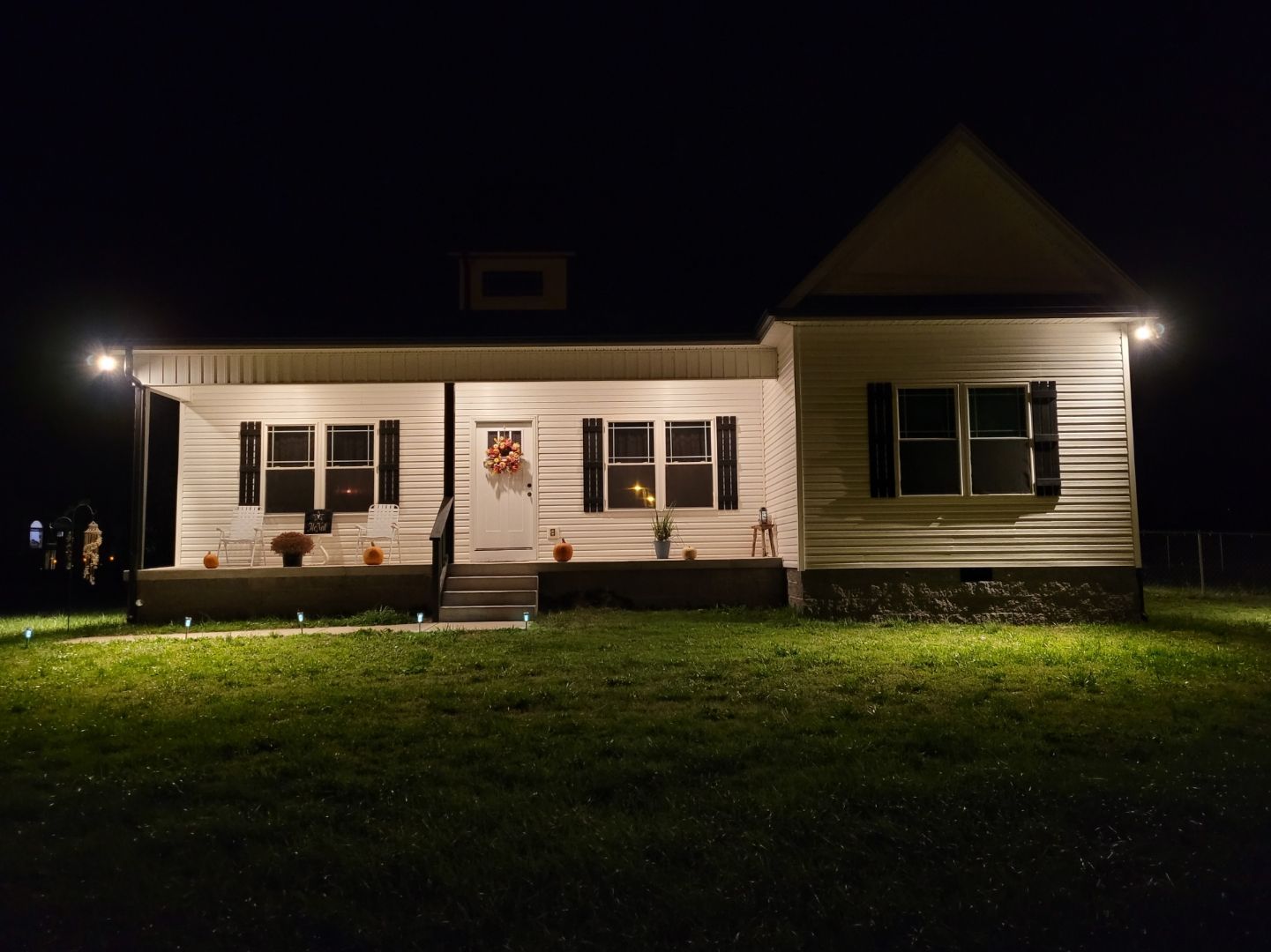 A white house is lit up at night with a porch.