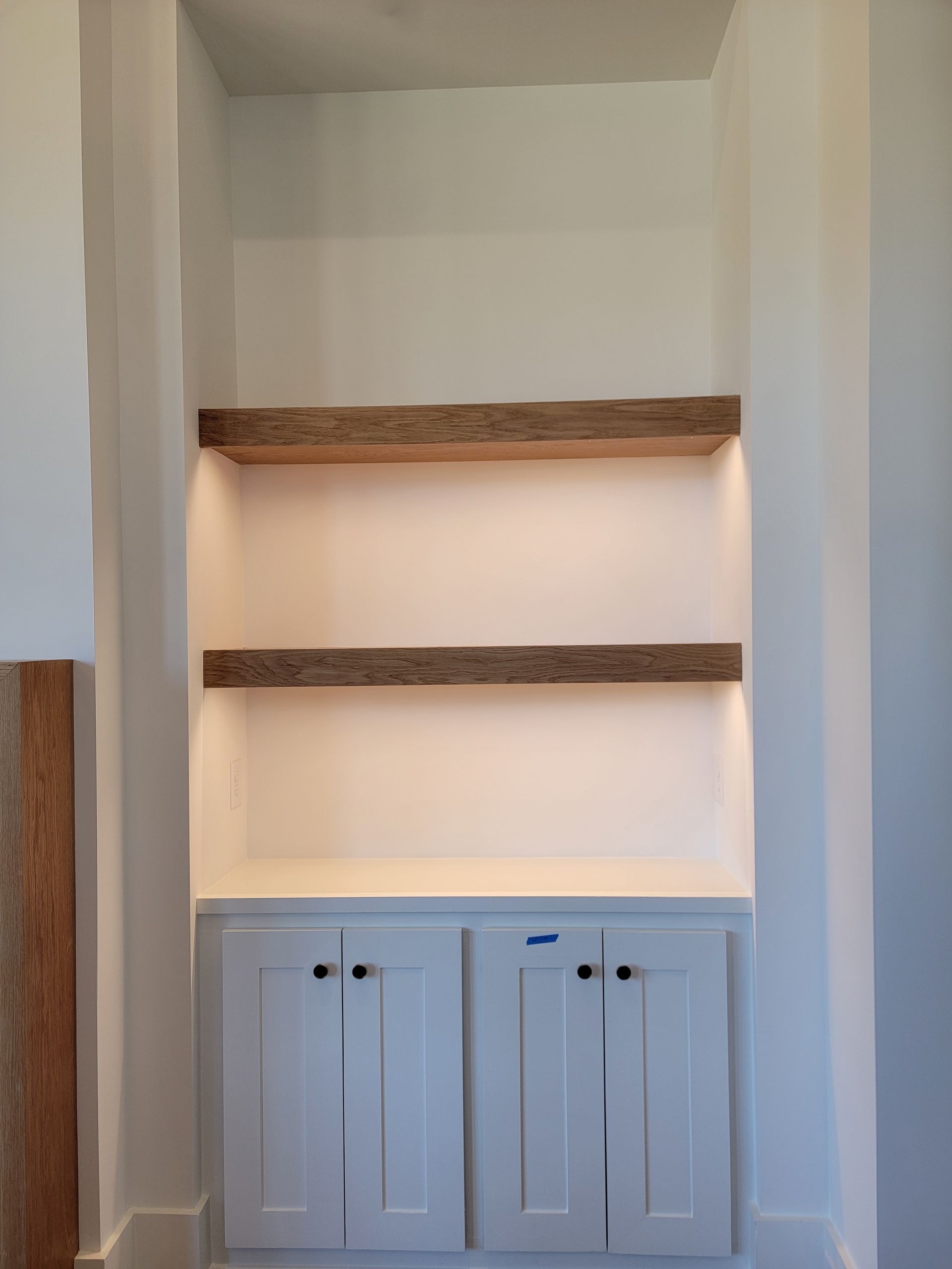 Built-in white cabinet with two wooden shelves, lit from above.