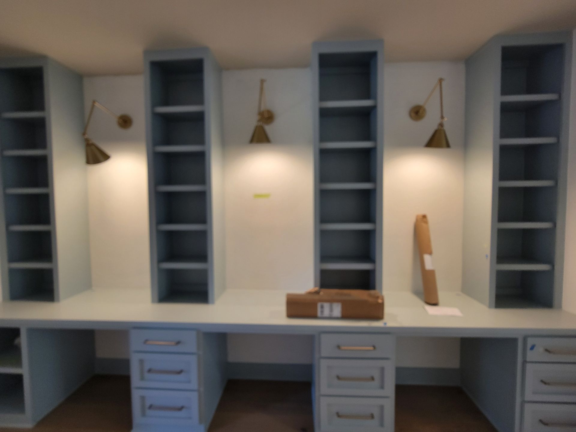 Light blue built-in desks with matching shelves, cabinets, and brass sconces against a white wall.