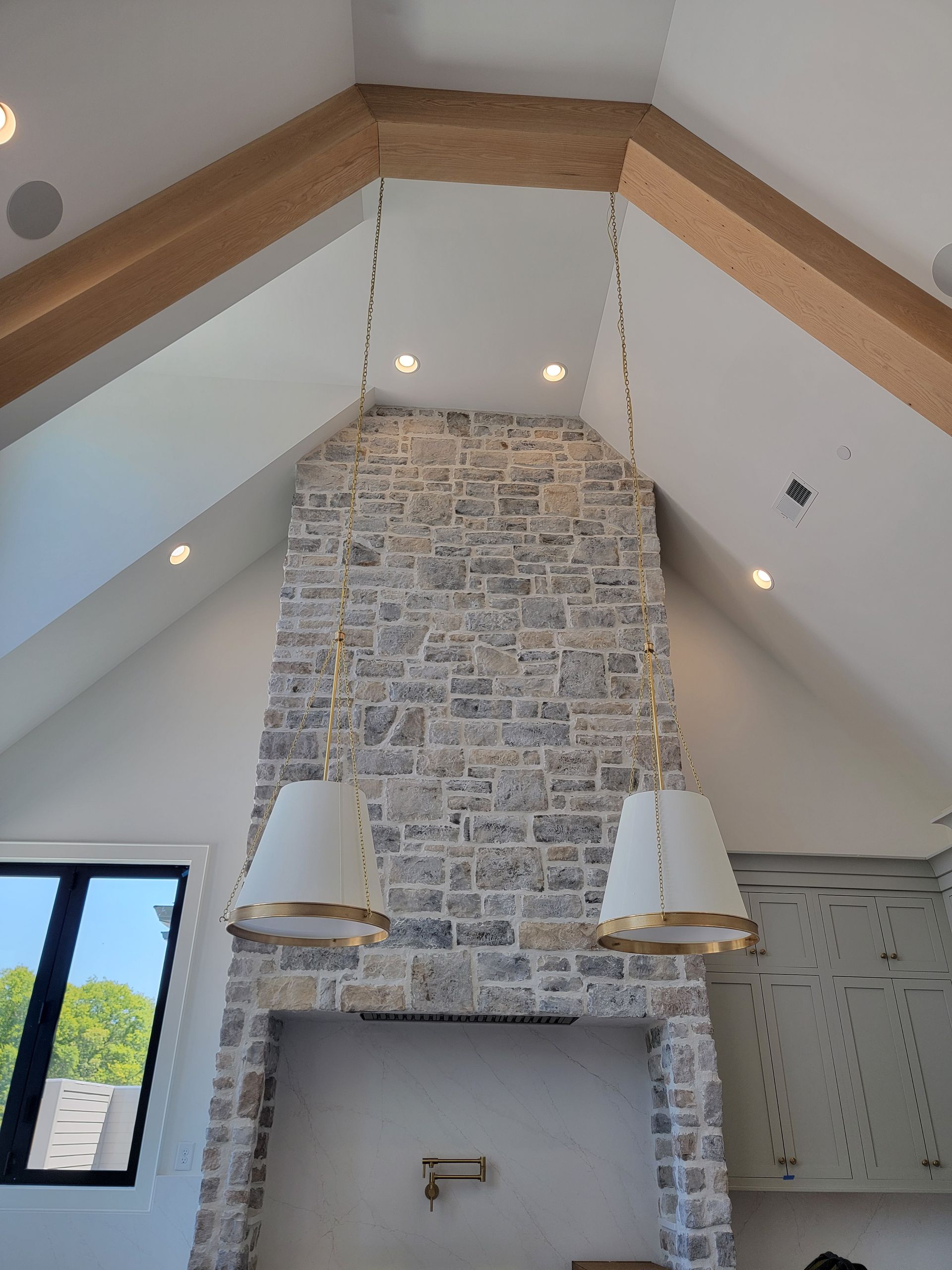 Stone fireplace with white lamps, recessed lights, and exposed wood beams in a bright room.