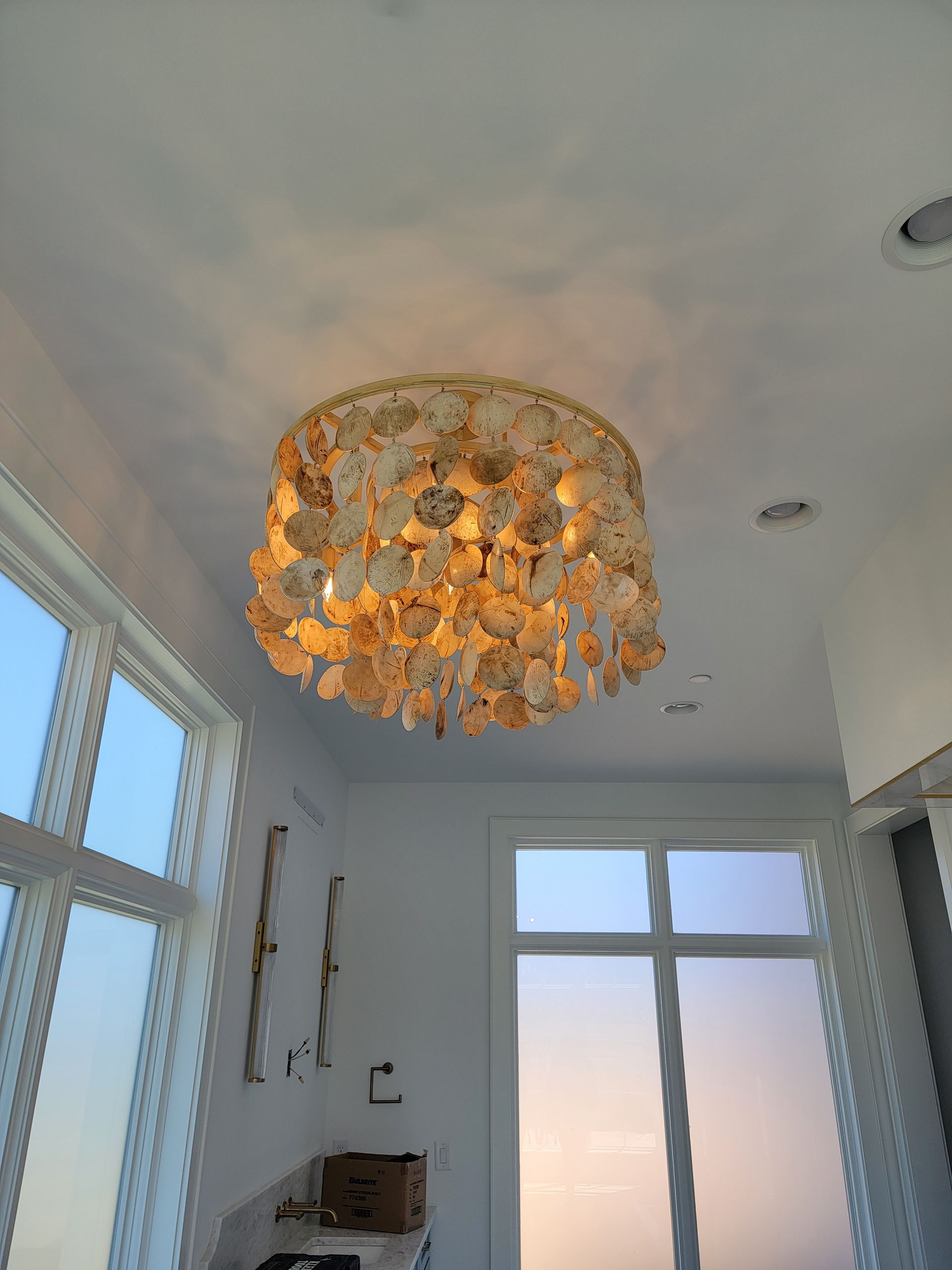Shell chandelier hanging in a bright room with windows and white walls.