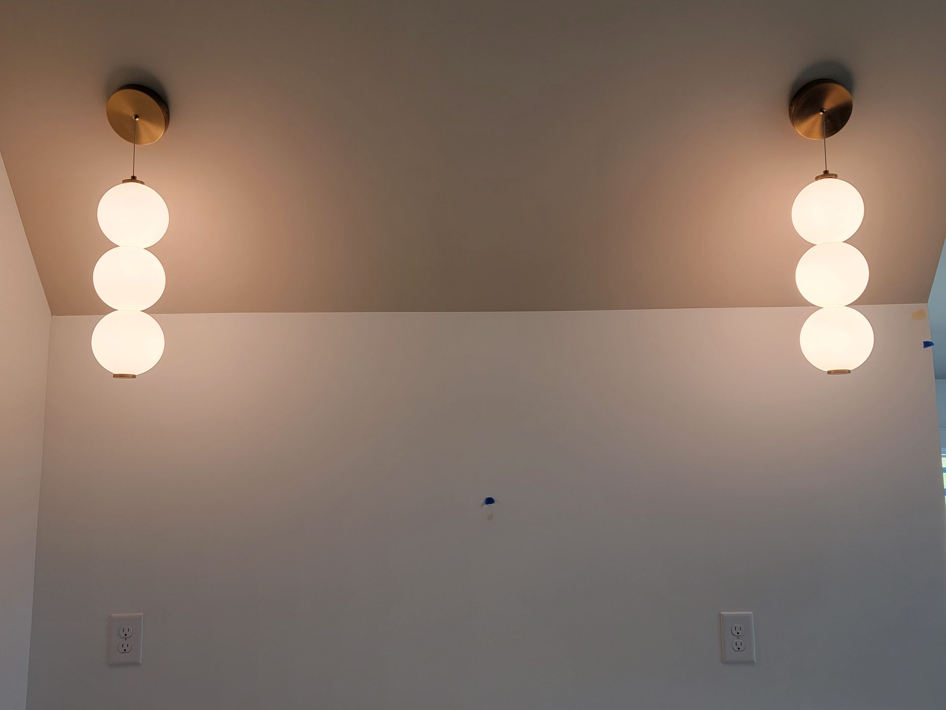 Two pendant lights with three white globes hang from a white ceiling over a white wall.