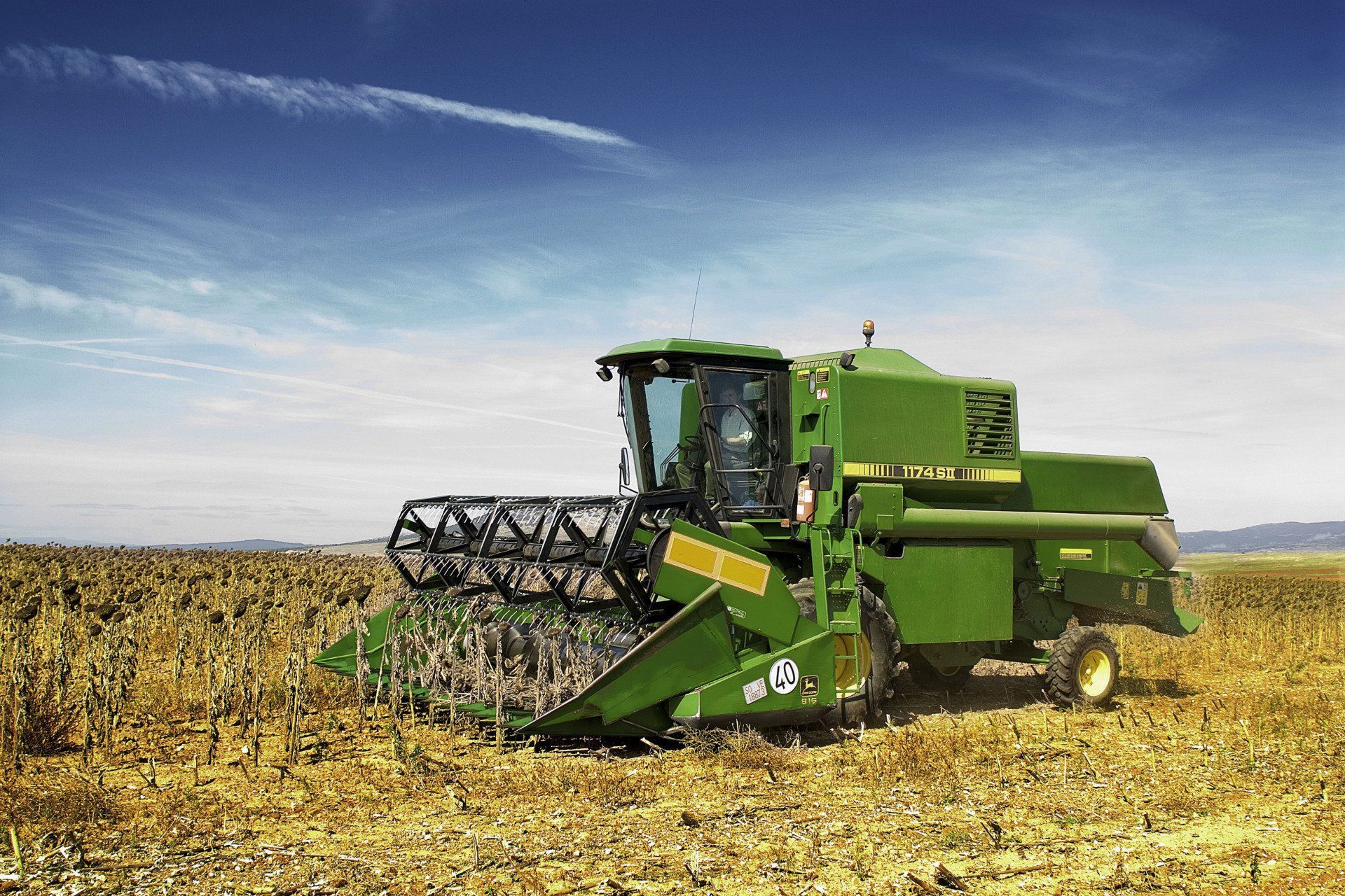 Green John Deere combine harvesting crops in a field under a blue sky.