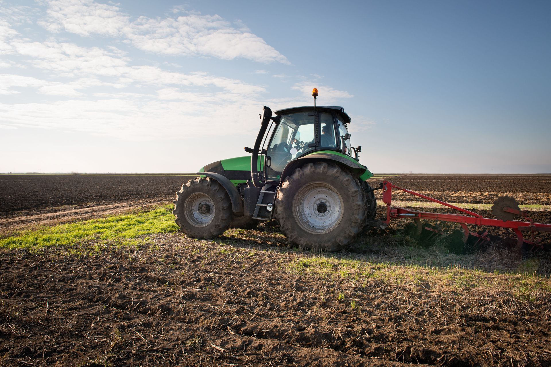 Green tractor plowing a brown field under a blue sky.