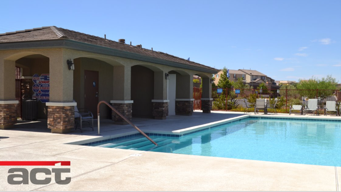Poolside building with a swimming pool and chairs on a sunny day. Building has arched entryways and brown and beige accents.