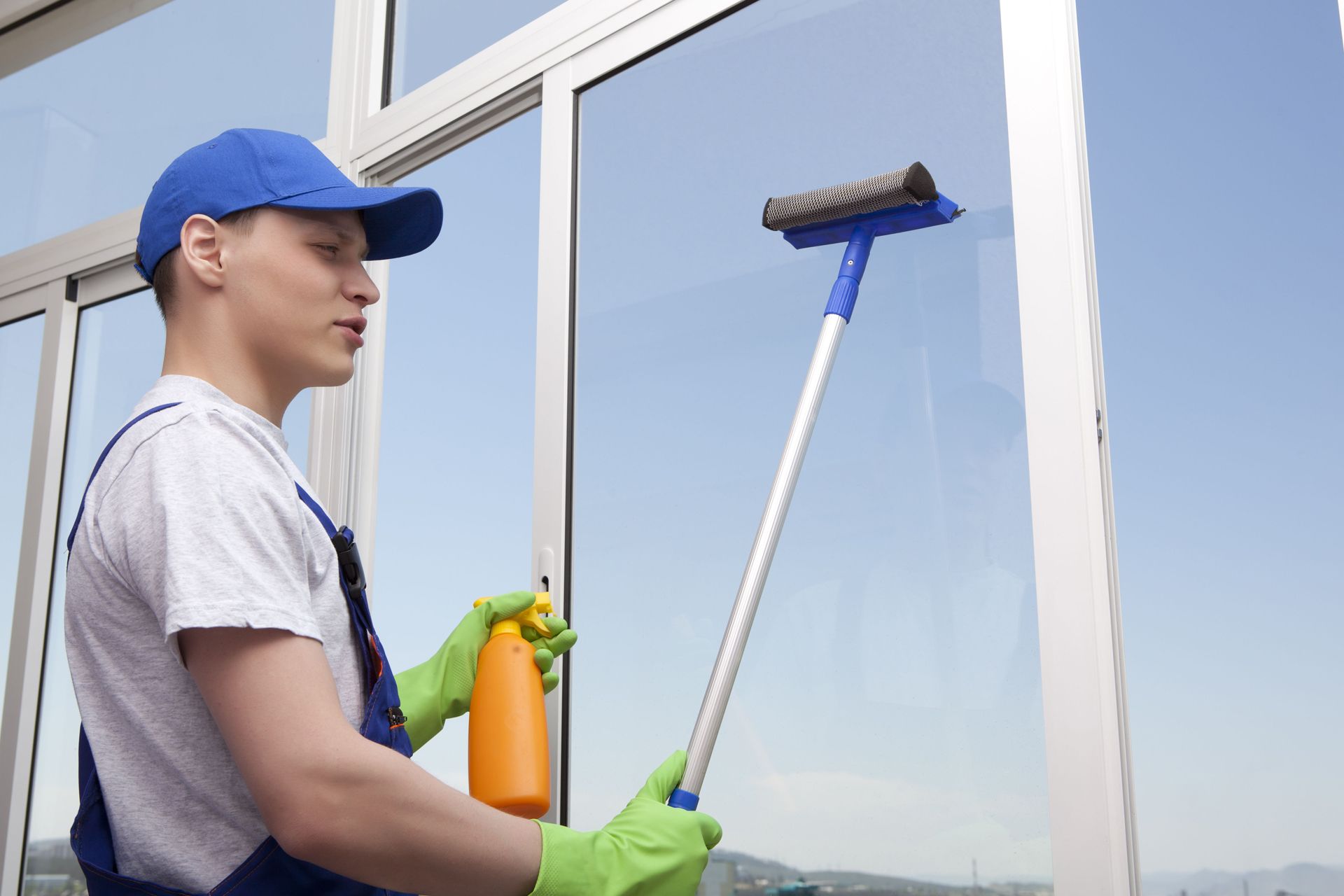A man is cleaning a window with a mop and spray bottle.