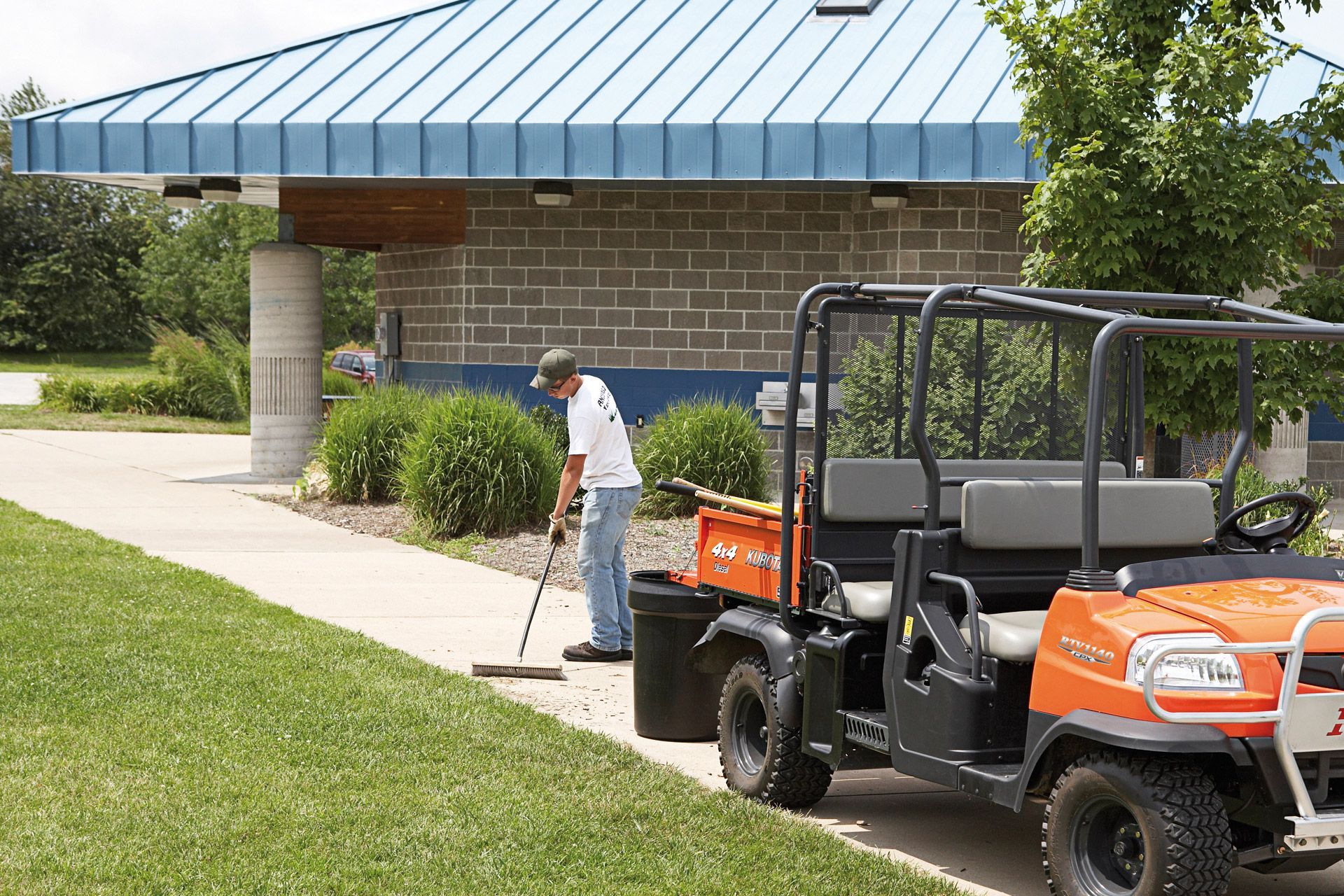 A man is sweeping the sidewalk next to an orange vehicle