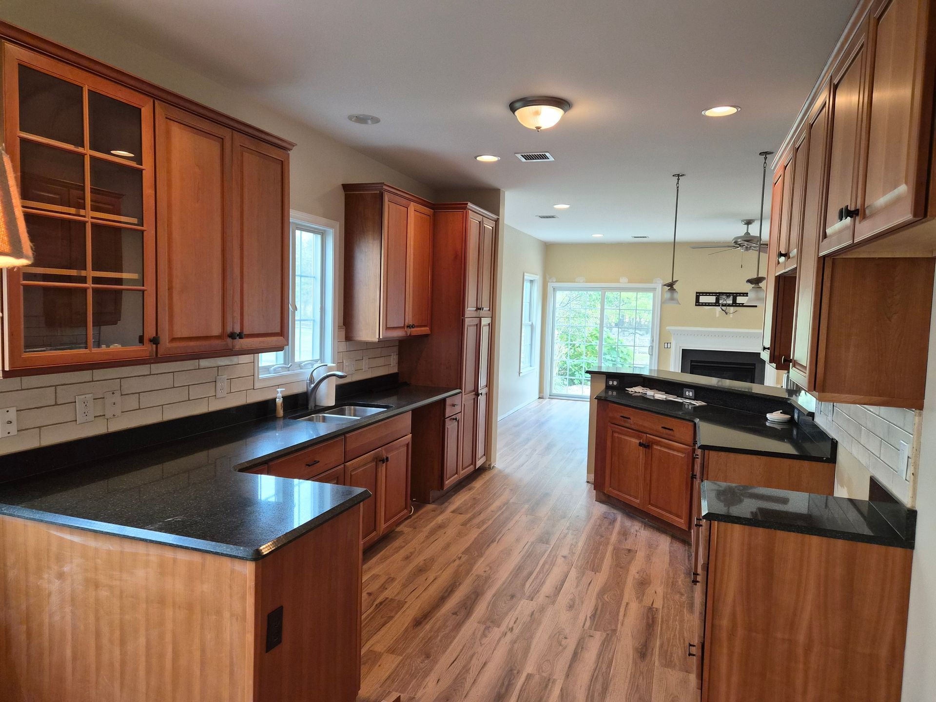 Kitchen with wood cabinets, dark countertops, and light wood-look floors.  A doorway leads to a living area.