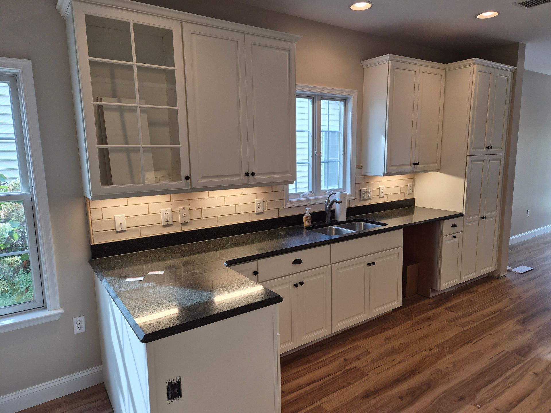 White kitchen cabinets with black countertops and wood flooring.