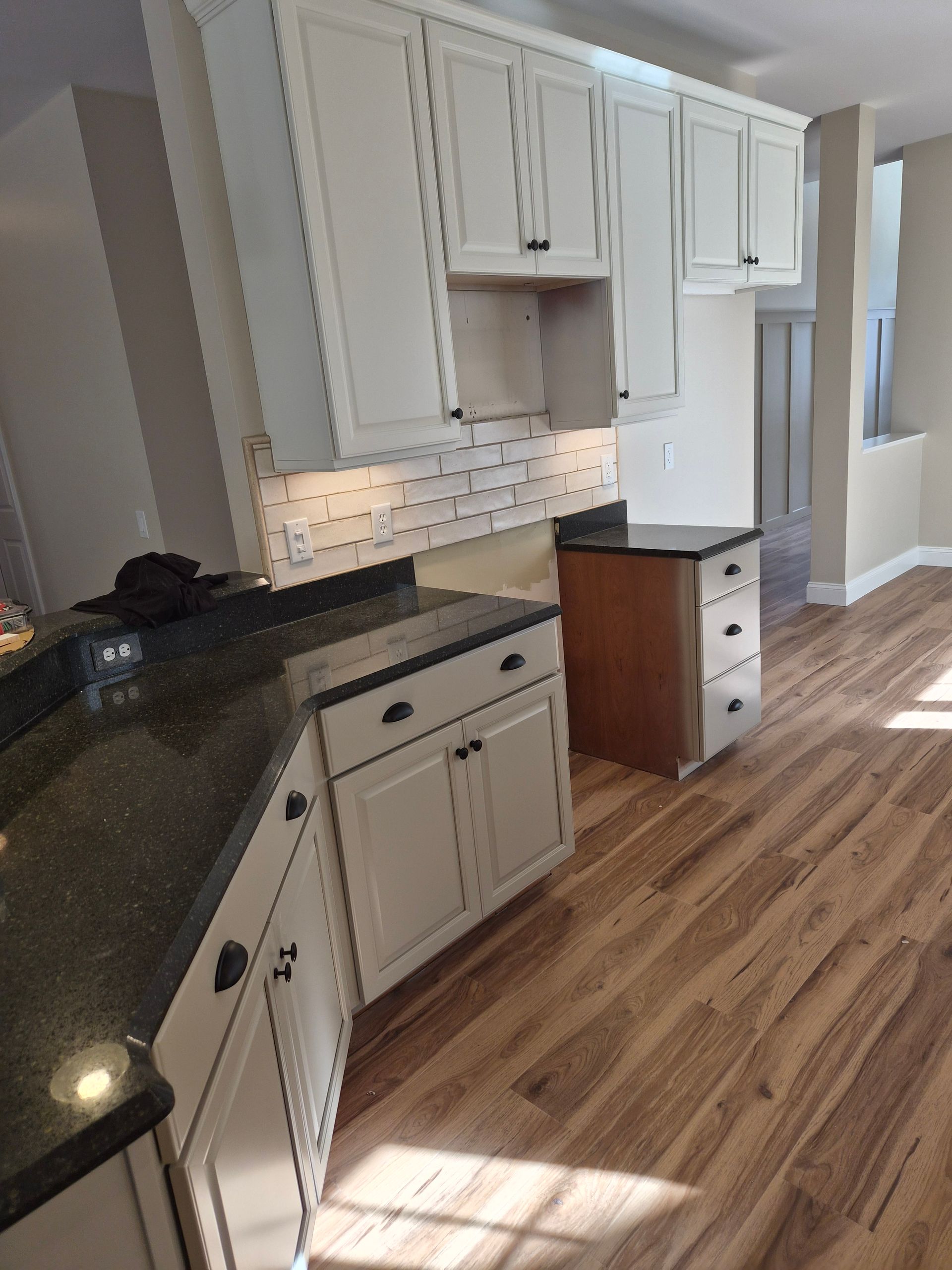 Kitchen with white cabinets, dark countertops, and wood flooring.