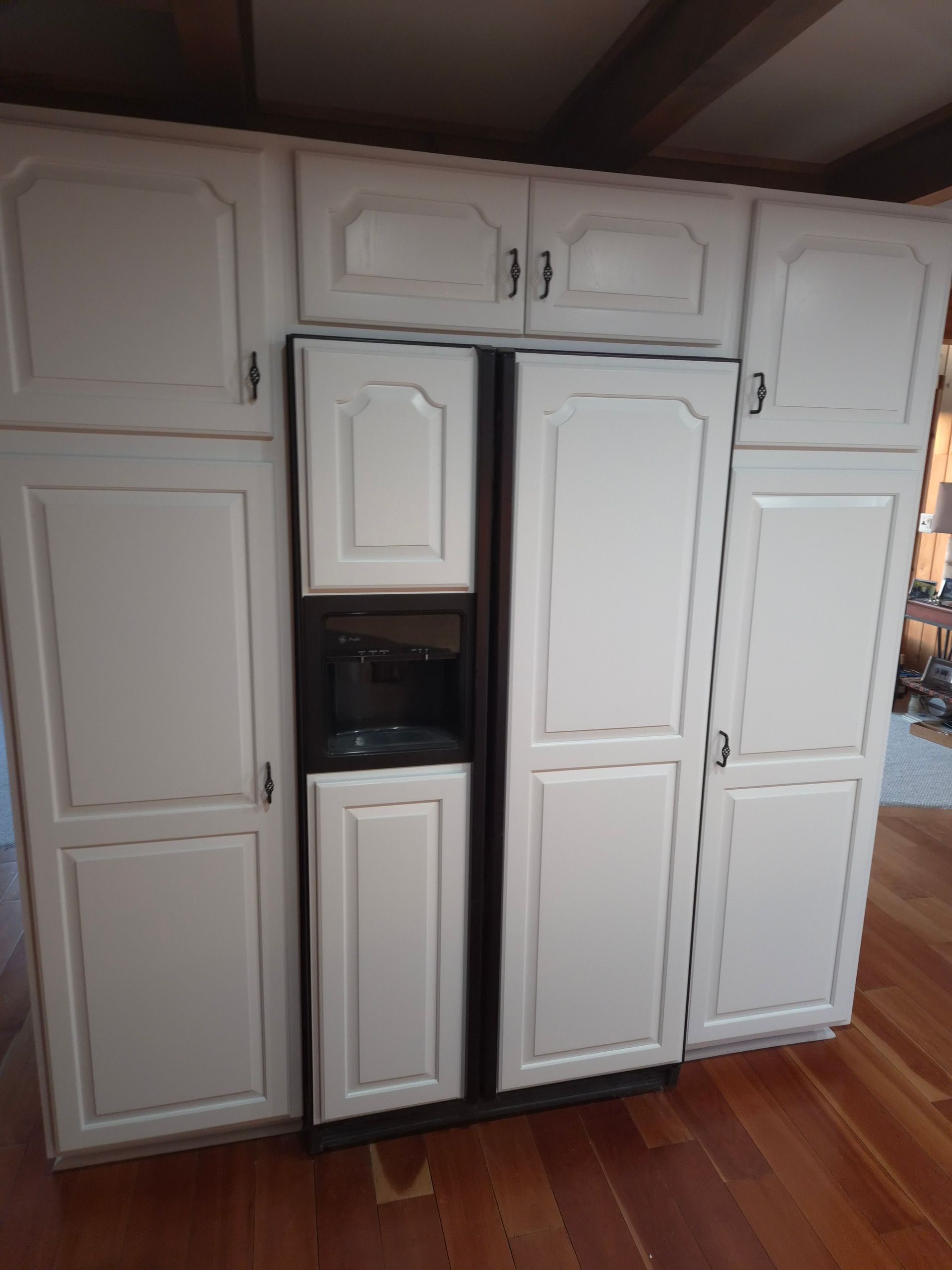 White kitchen cabinets surrounding a dark appliance with a water/ice dispenser on a hardwood floor.
