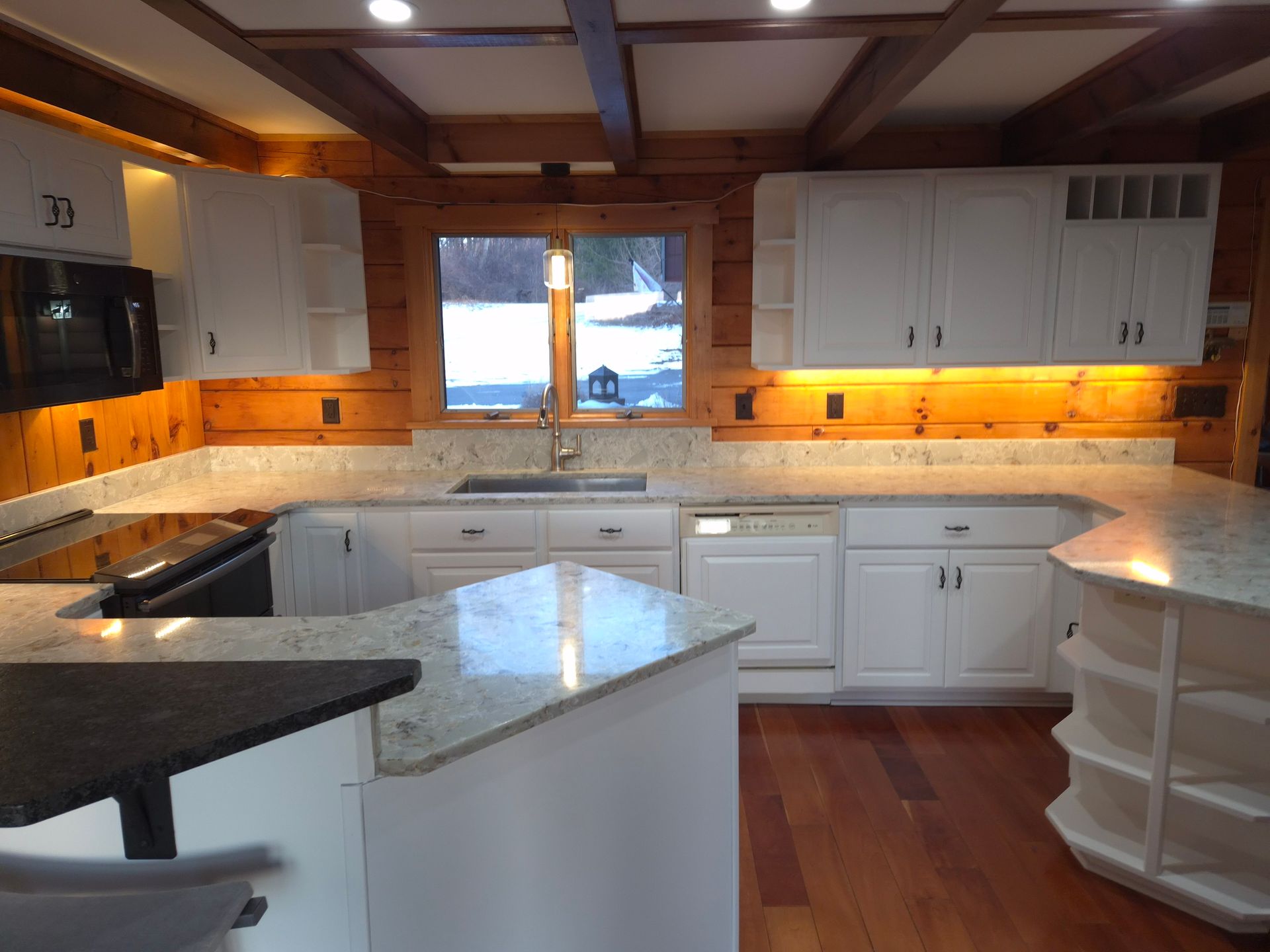 Kitchen with white cabinets, wood paneling, granite countertops, and a window overlooking snow.