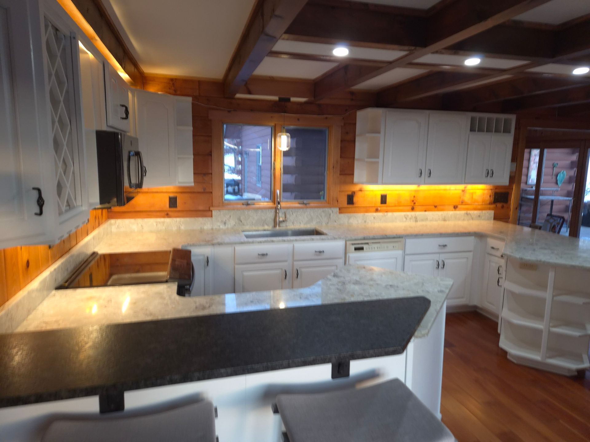 White kitchen with wood accents, granite countertops, and under-cabinet lighting.
