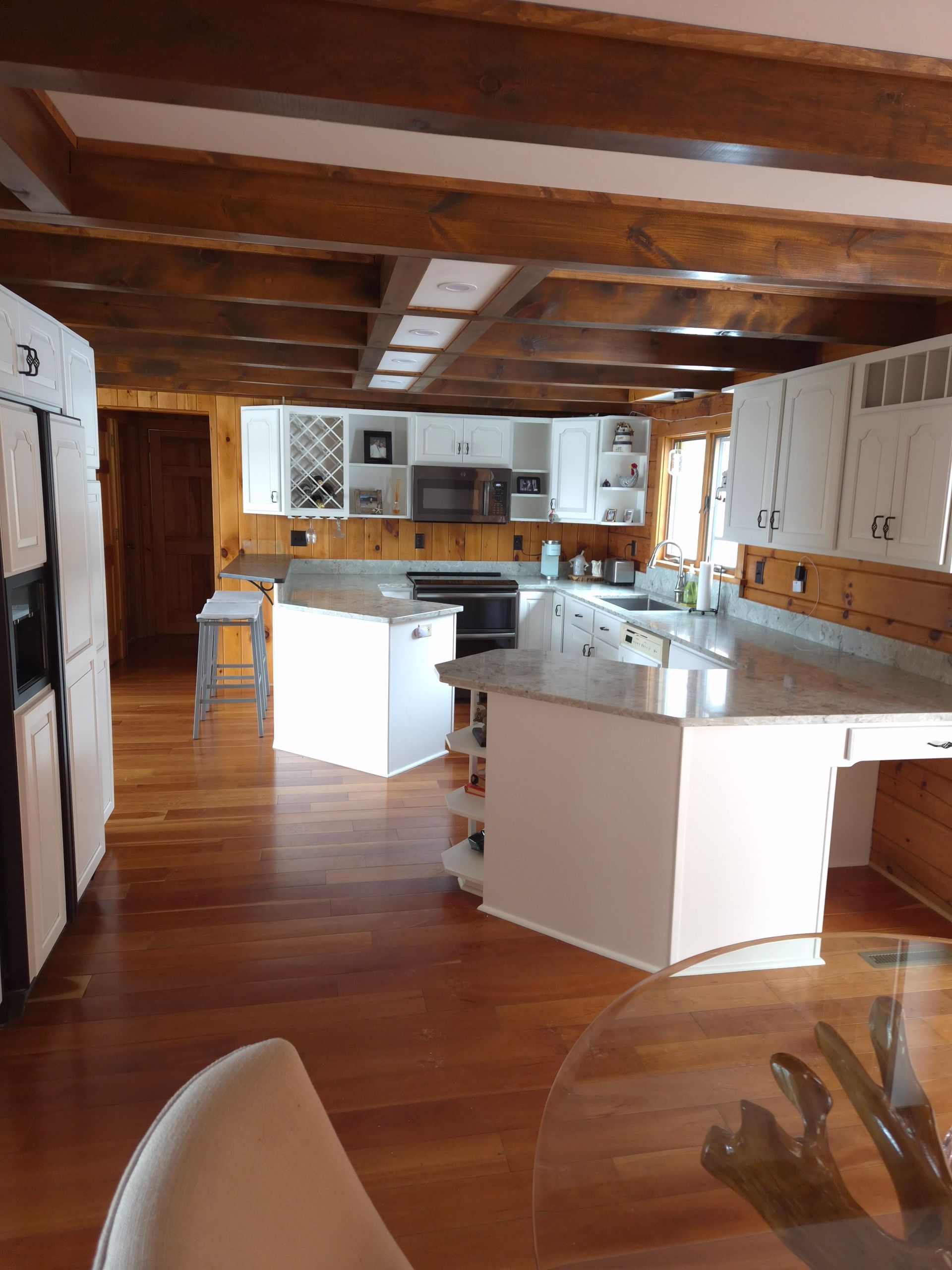 Spacious kitchen with wood beams, white cabinets, and two islands. Hardwood floors and bright lighting.