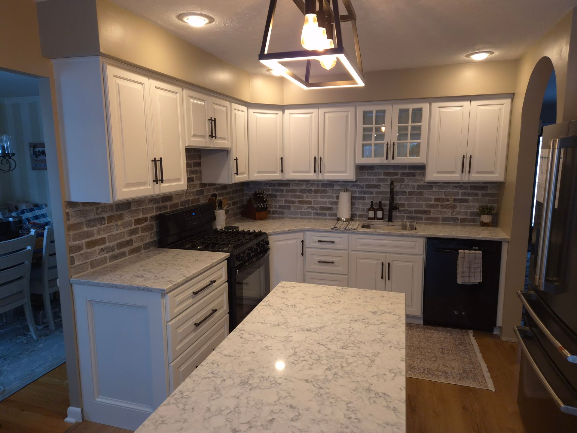 White kitchen with granite countertops, brick backsplash, black appliances, and a central island.