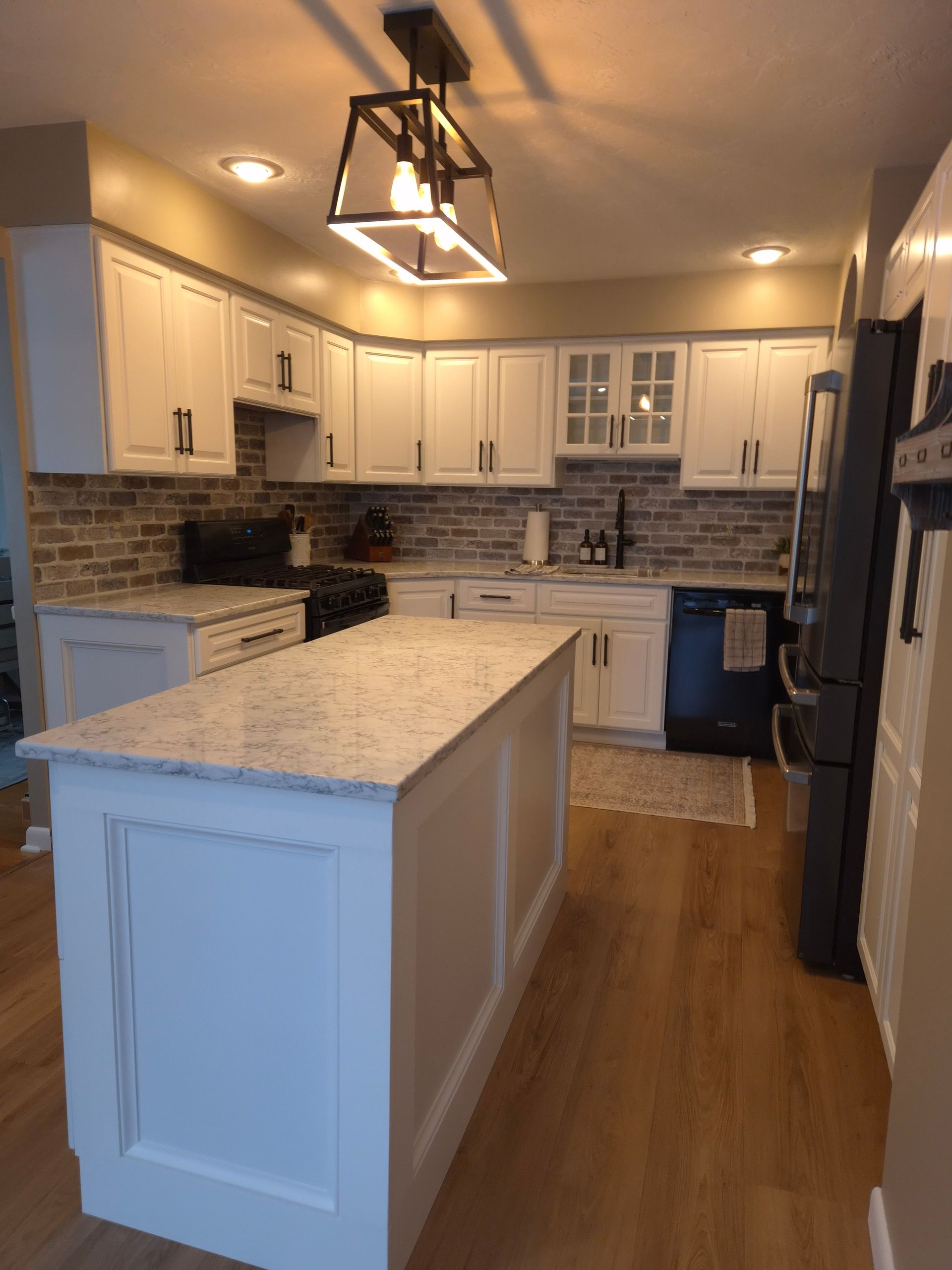 Modern white kitchen with island, wood floor, and backsplash.